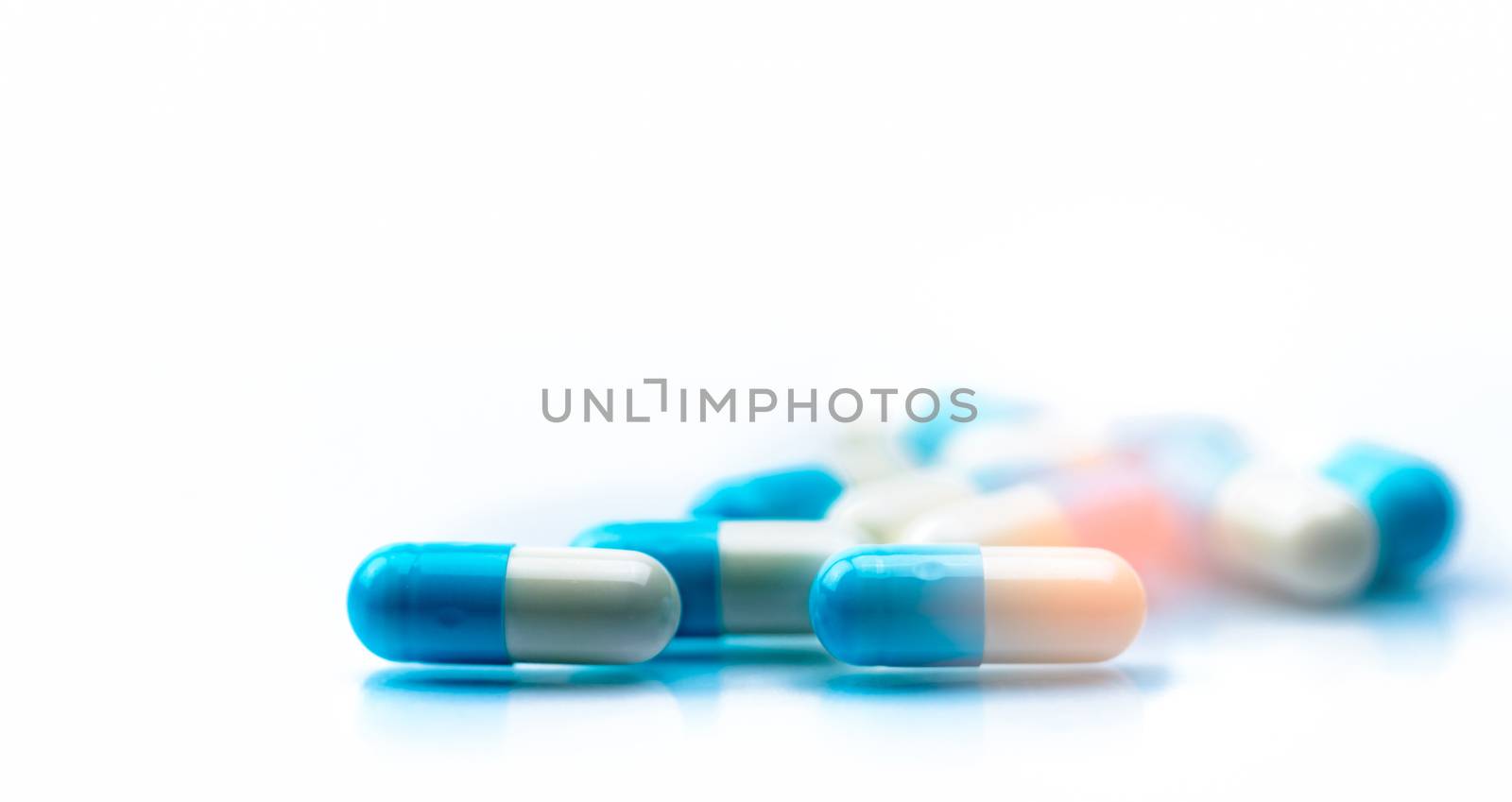 Selective focus on blue and white capsules pill spread on white background with shadow. Global healthcare concept. Antibiotics drug resistance. Antimicrobial capsule pills. Pharmaceutical industry. by Fahroni