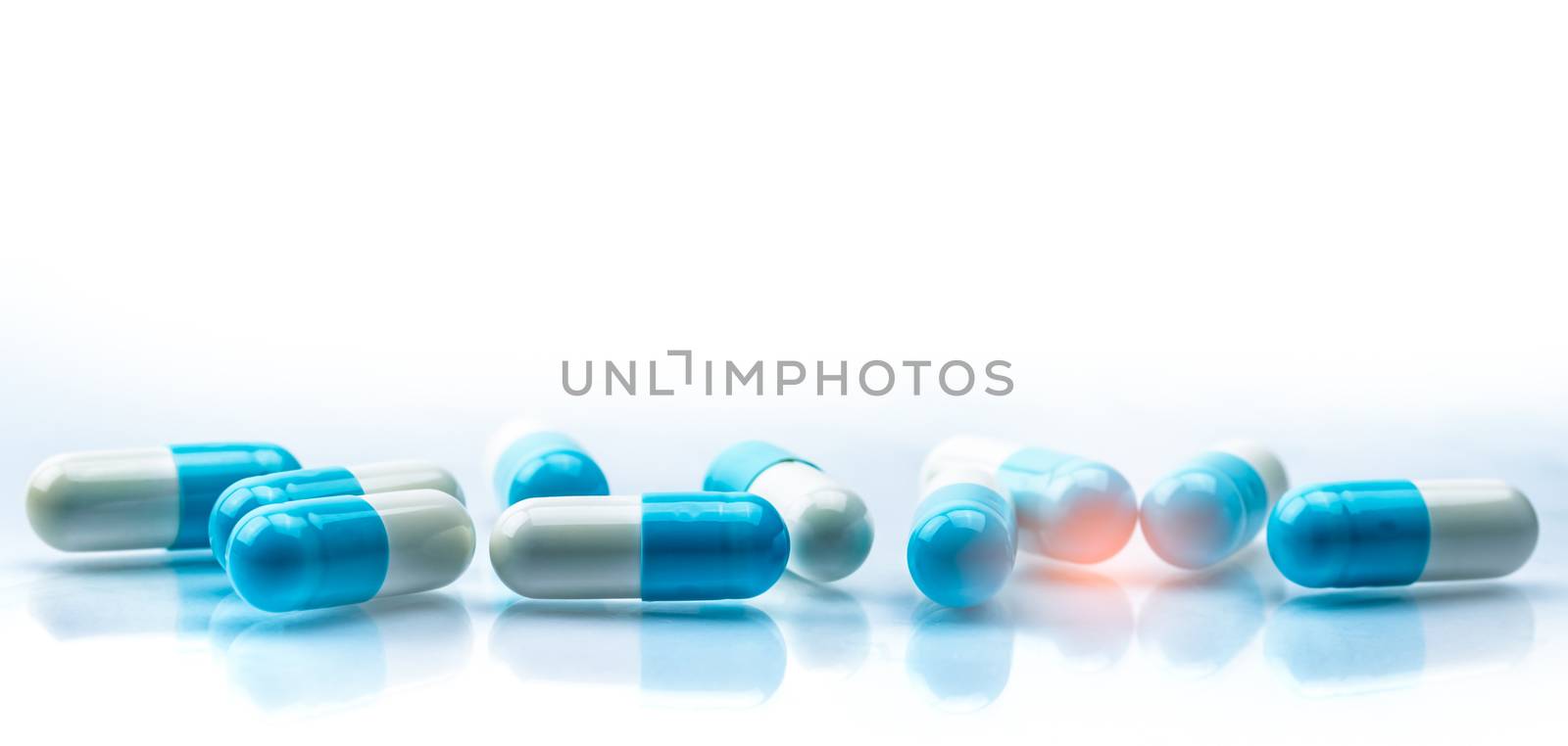 Blue and white capsules pill spread on white background with shadow and copy space. Global healthcare concept. Antibiotics drug resistance. Antimicrobial capsule pills. Pharmaceutical industry. by Fahroni