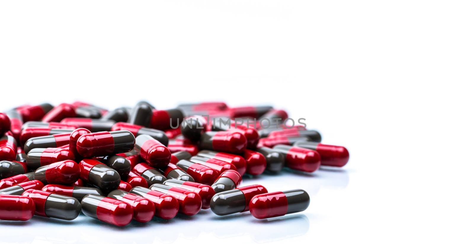 Pile of red and grey capsule pills isolated on white background with copy space. Flunarizine : drug for migraine prophylaxis treatment. Global healthcare concept. Pharmaceutical industry