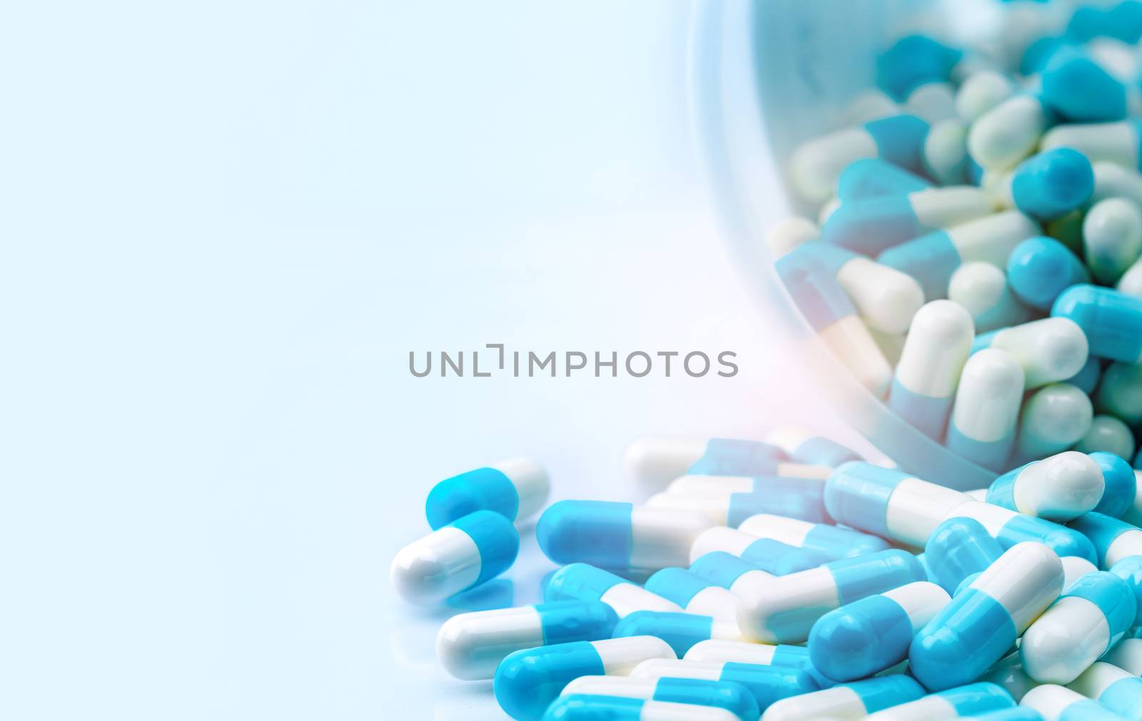 Blue and white capsules pill spilled out from white plastic bottle container. Global healthcare concept. Antibiotics drug resistance. Antimicrobial capsule pills. Pharmaceutical industry. by Fahroni