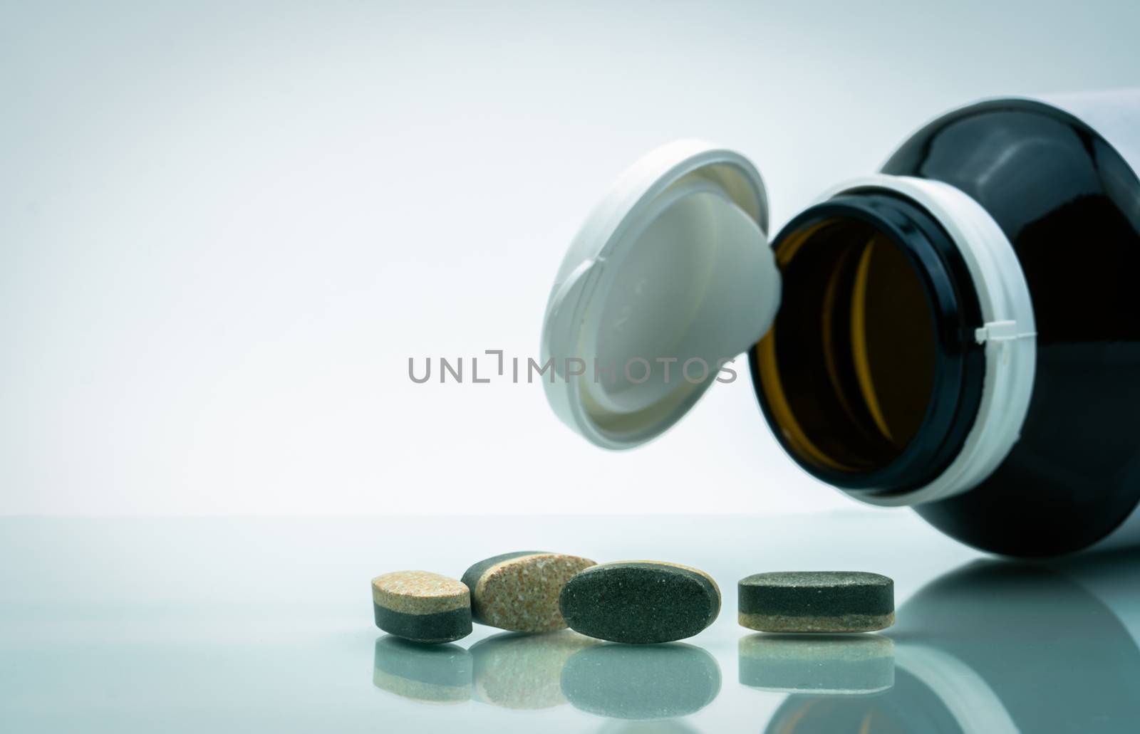 Essential Vitamins and minerals supplements dual layer tablet pills and medicine glass bottle with open cap isolated on white background with copy space. Use for vitamins and supplements advertising.