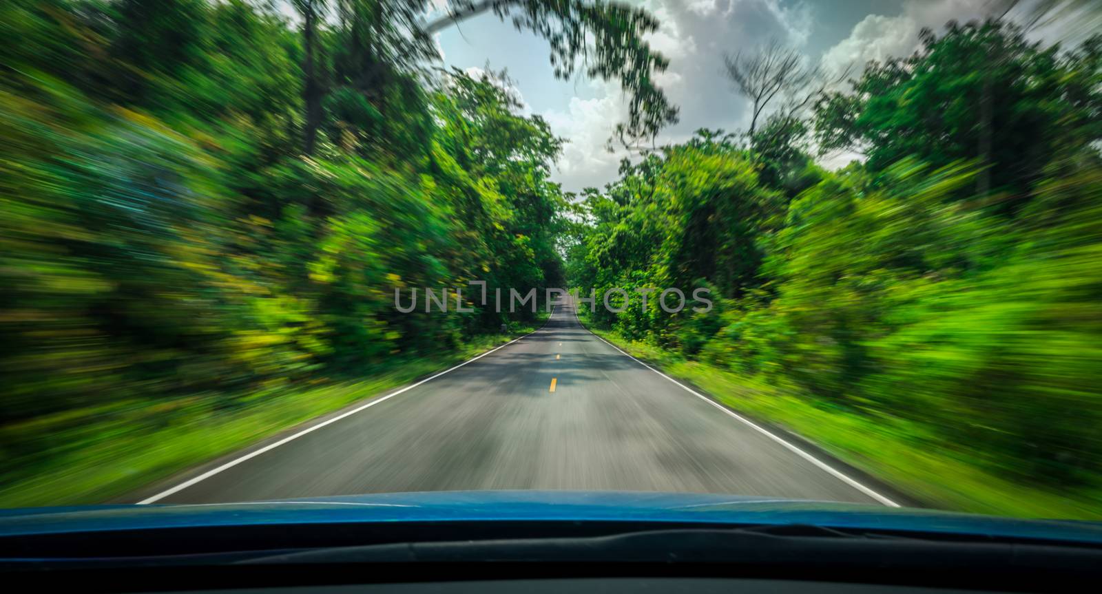 View from front of blue car on asphalt road and speed motion blur on highway in summer with green trees forest at countryside