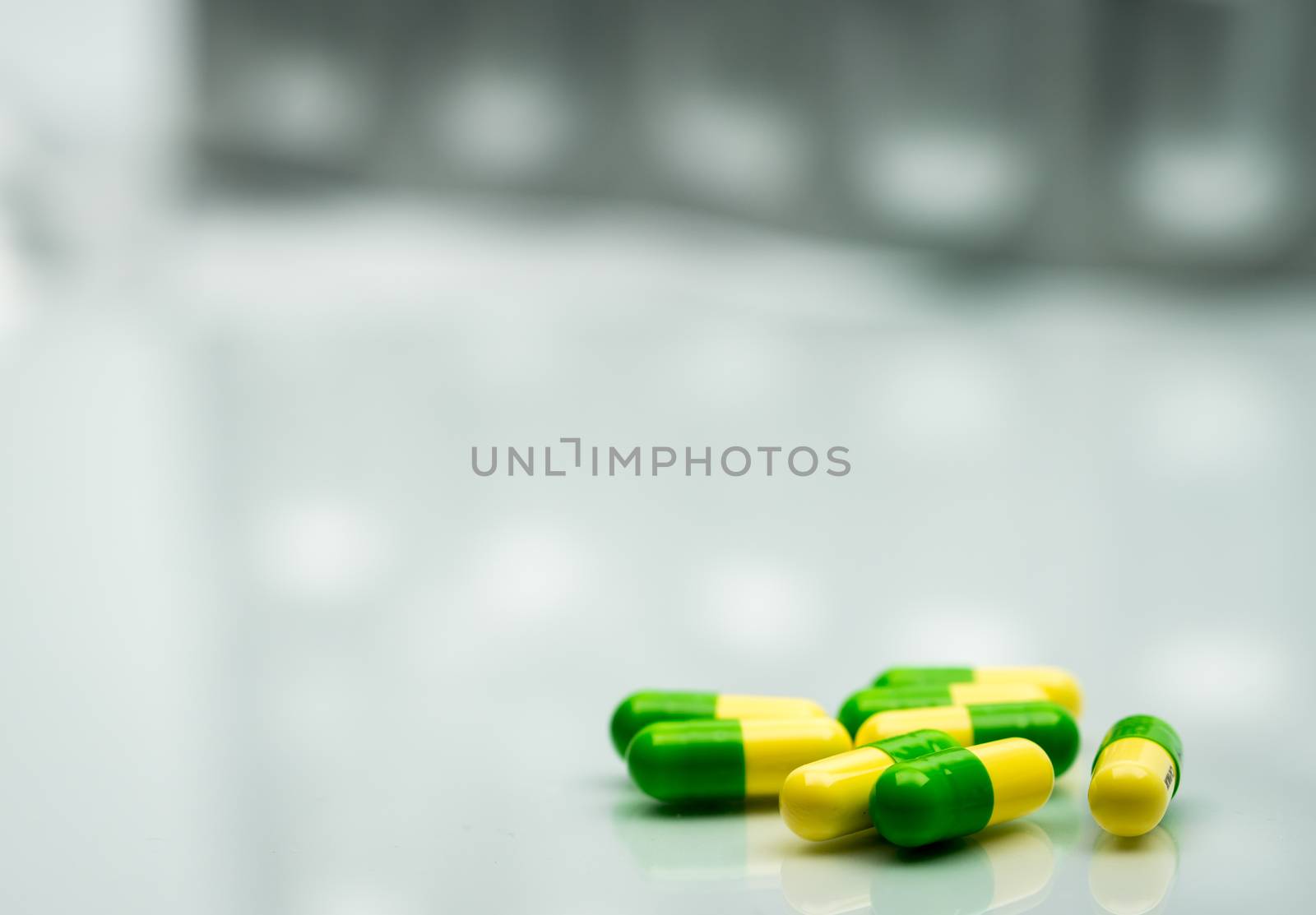 Green, yellow tramadol capsule pills on blurred silver blister pack background with copy space. Cancer pain management. Opioid analgesics. Drug abuse in teenage. Pharmaceutical industry. Pharmacy background. Global healthcare concept. by Fahroni