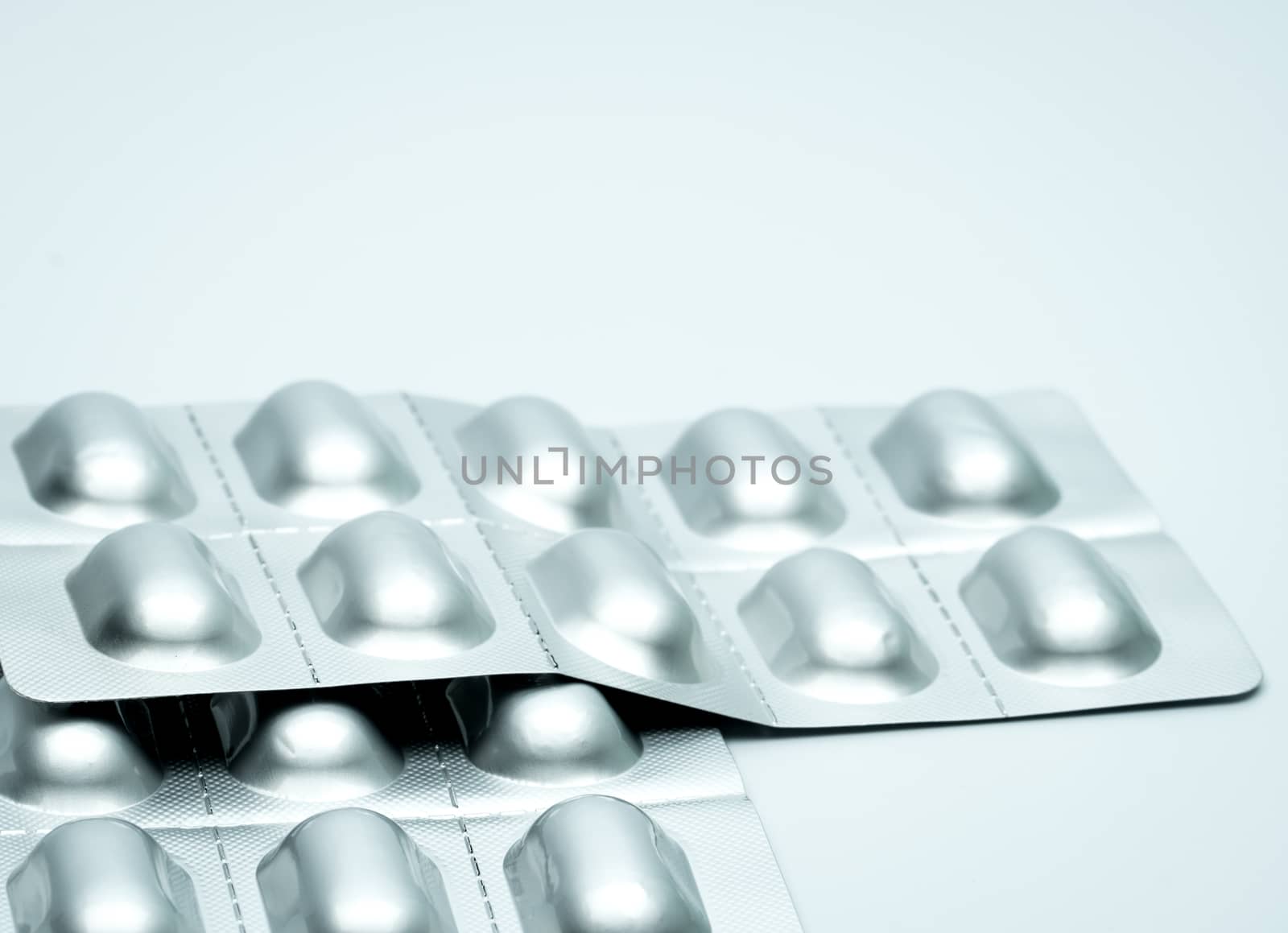 Tablet pills in silver aluminium blister pack packaging on blurred background of pack of pills with copy space. Pharmaceutical industry. Pharmacy background. Global healthcare concept. Health budgets and policy concept.