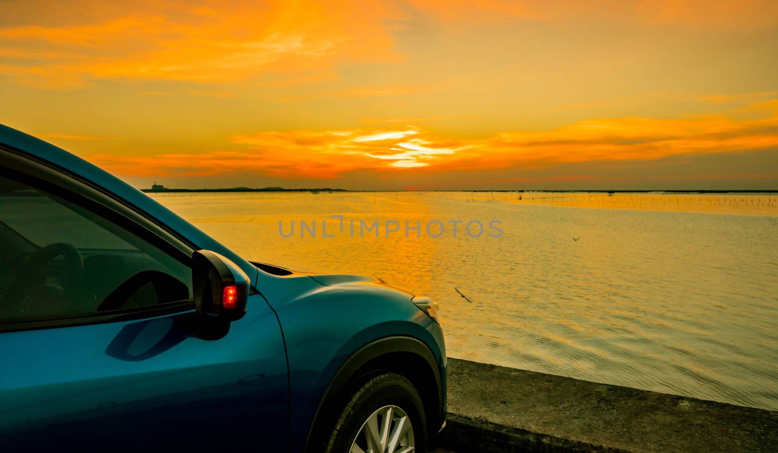 Blue compact SUV car with sport and modern design parked on concrete road by the sea at sunset. Environmentally friendly technology. Business success concept. by Fahroni