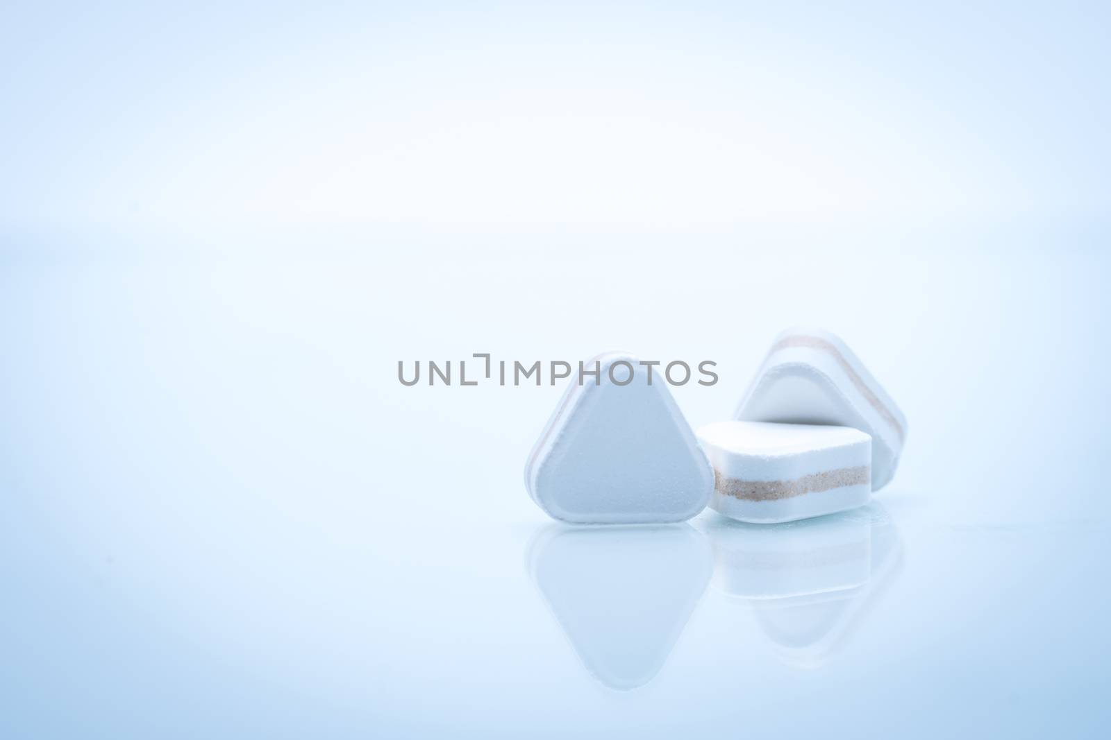 Macro shot of triangle shape tablet pills. Three layers tablet pills for indication antacid, digestive and gastric pain. Group of sandwich tablets pills on white background with copy space for text. Pharmaceutical industry. Pharmacy background.