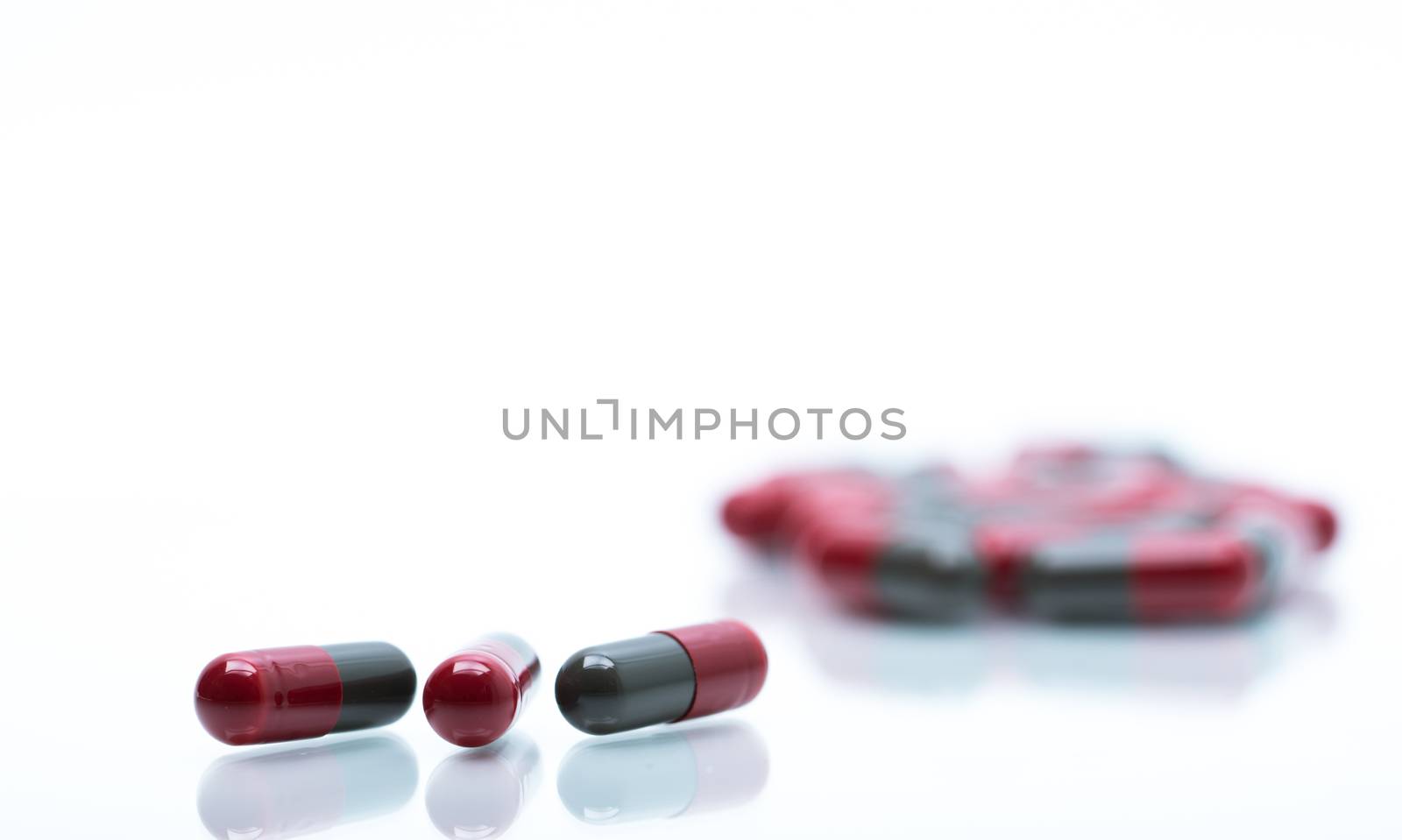 Macro shot detail selective focus of red and grey capsule pills on white background with blurred capsule. Migraine prophylaxis treatment concept. Pharmaceutical industry. Pharmacy background. Global healthcare concept.