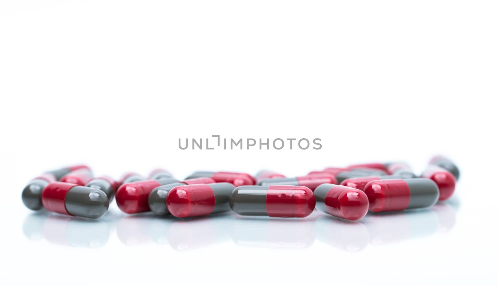 Macro shot detail selective focus of red and grey capsule pills isolated on white background with copy space for text. Migraine prophylaxis treatment concept. Pharmaceutical industry. Pharmacy background. Global healthcare concept. by Fahroni