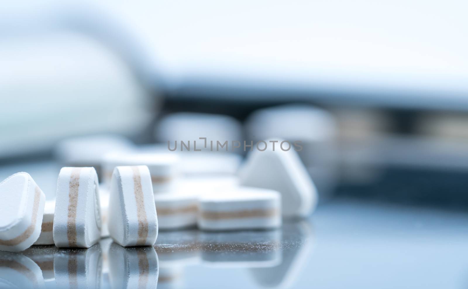 Macro shot of triangle shape tablet pills. Three layers tablet pills for indication antacid, digestive and gastric pain. Group of sandwich tablets pills on stainless steel drug tray.
