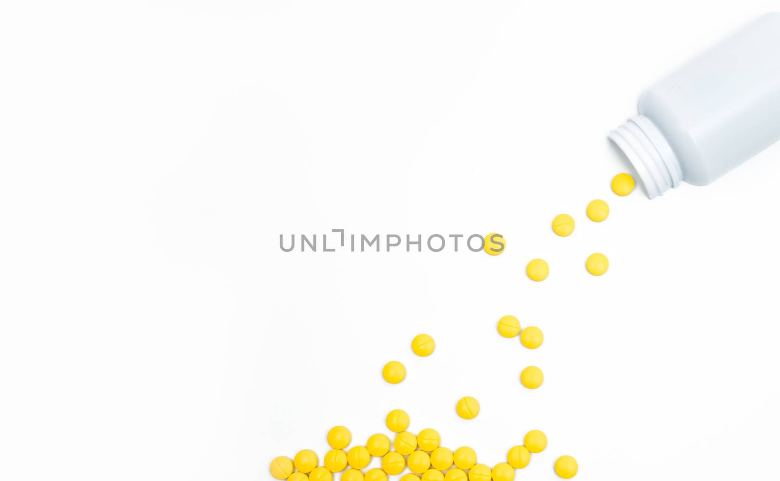 Yellow film coated tablets pills spilling out of pill bottle on white background with copy space. Painkiller tablet pills. NSAIDs pills for muscle pain. Pharmaceutical industry production. Pharmacy background. Global healthcare concept.