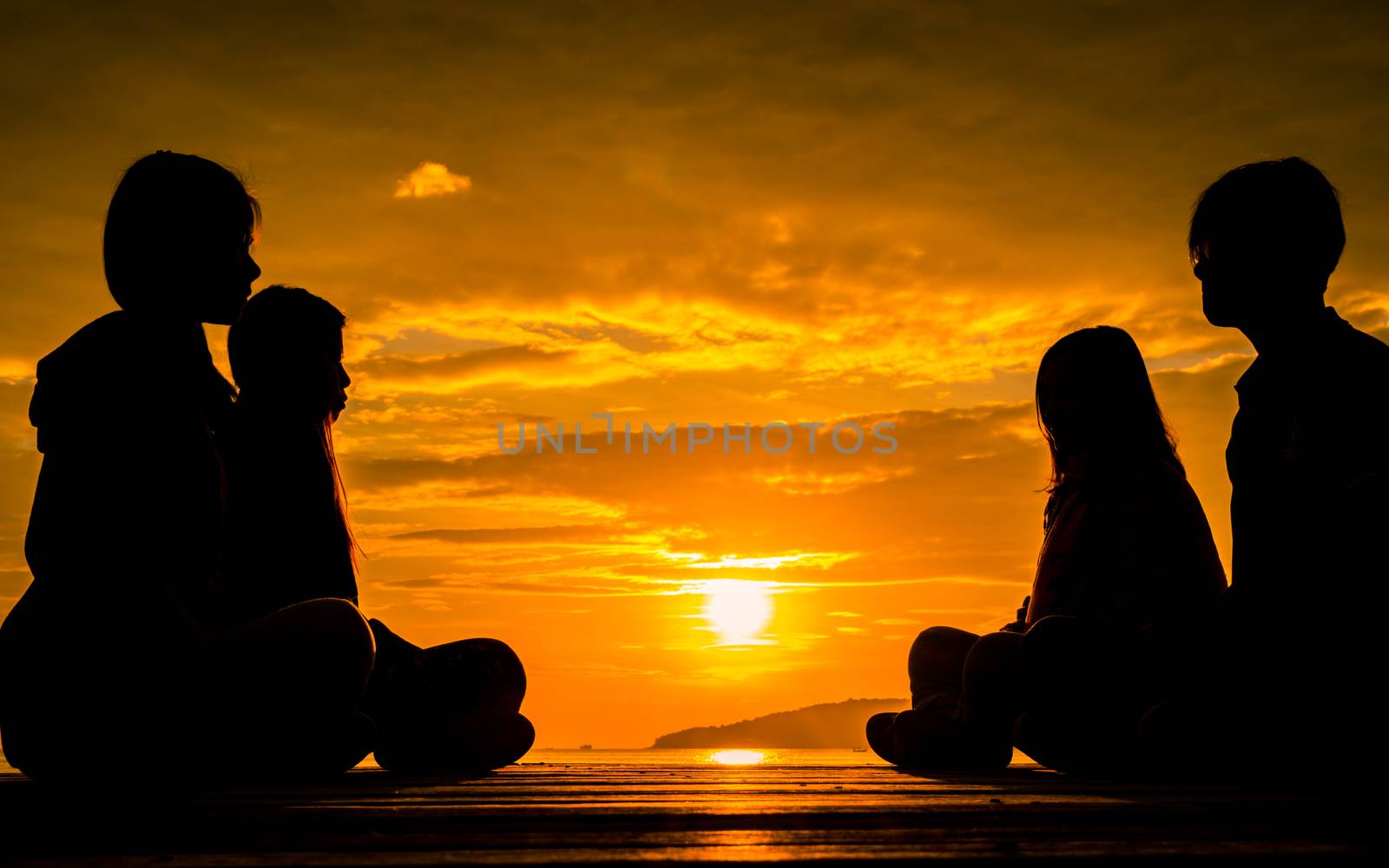 Four young people sit on wooden pier at sunrise on the beach to make meditation with orange  beautiful sky and clouds. by Fahroni