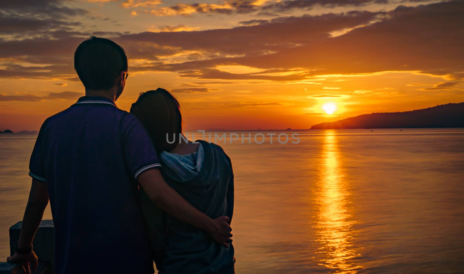 Silhouette of attractive young romantic couple in love is hugging on the beach at sunrise with beautiful golden sky. Vacation and travel concept. Romantic young couple dating at seaside. by Fahroni