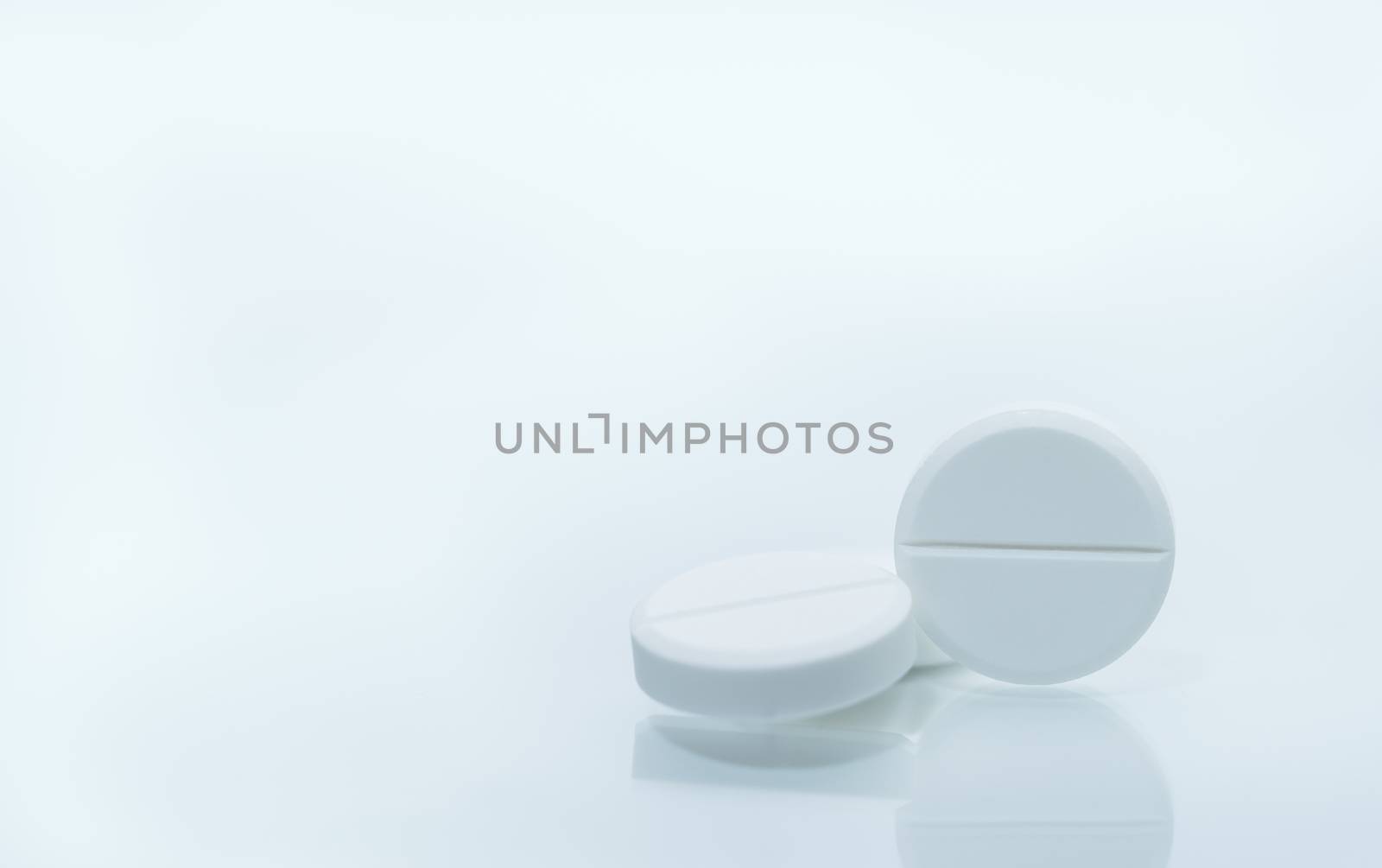 Macro shot of three white chewable tablets on white background with shadows. Antacids pills for relief stomachache from excess gastric acid in stomach. Stress induce gastric ulcer treatment concept. Pharmaceutical industry. Pharmacy background. Global healthcare concept. Health budgets and policy. by Fahroni