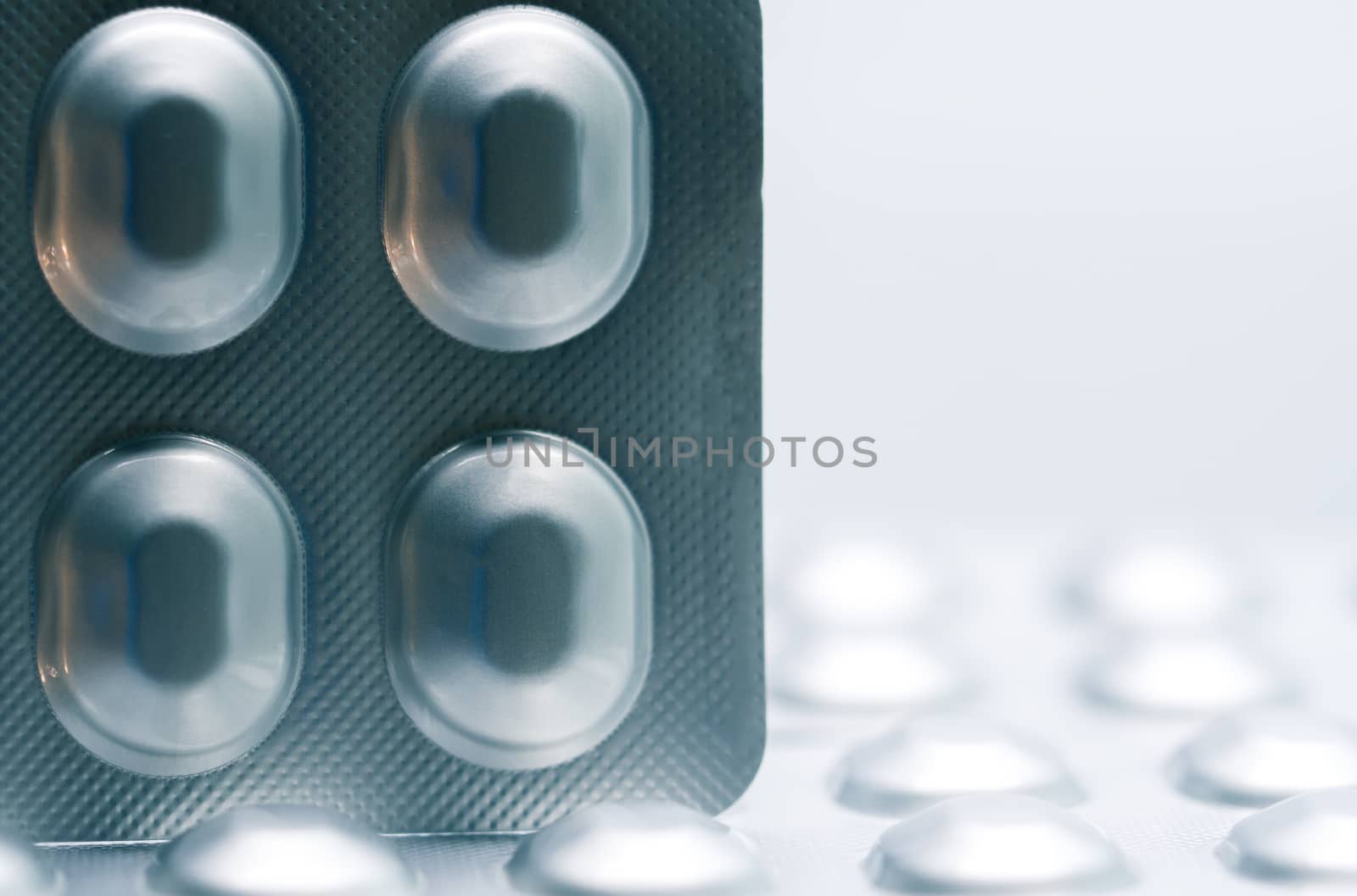 Macro shot detail of tablet pills in silver aluminium blister pack packaging on blurred background of pack of pills. Pharmaceutical industry. Pharmacy background. Global healthcare concept. Health budgets and policy.