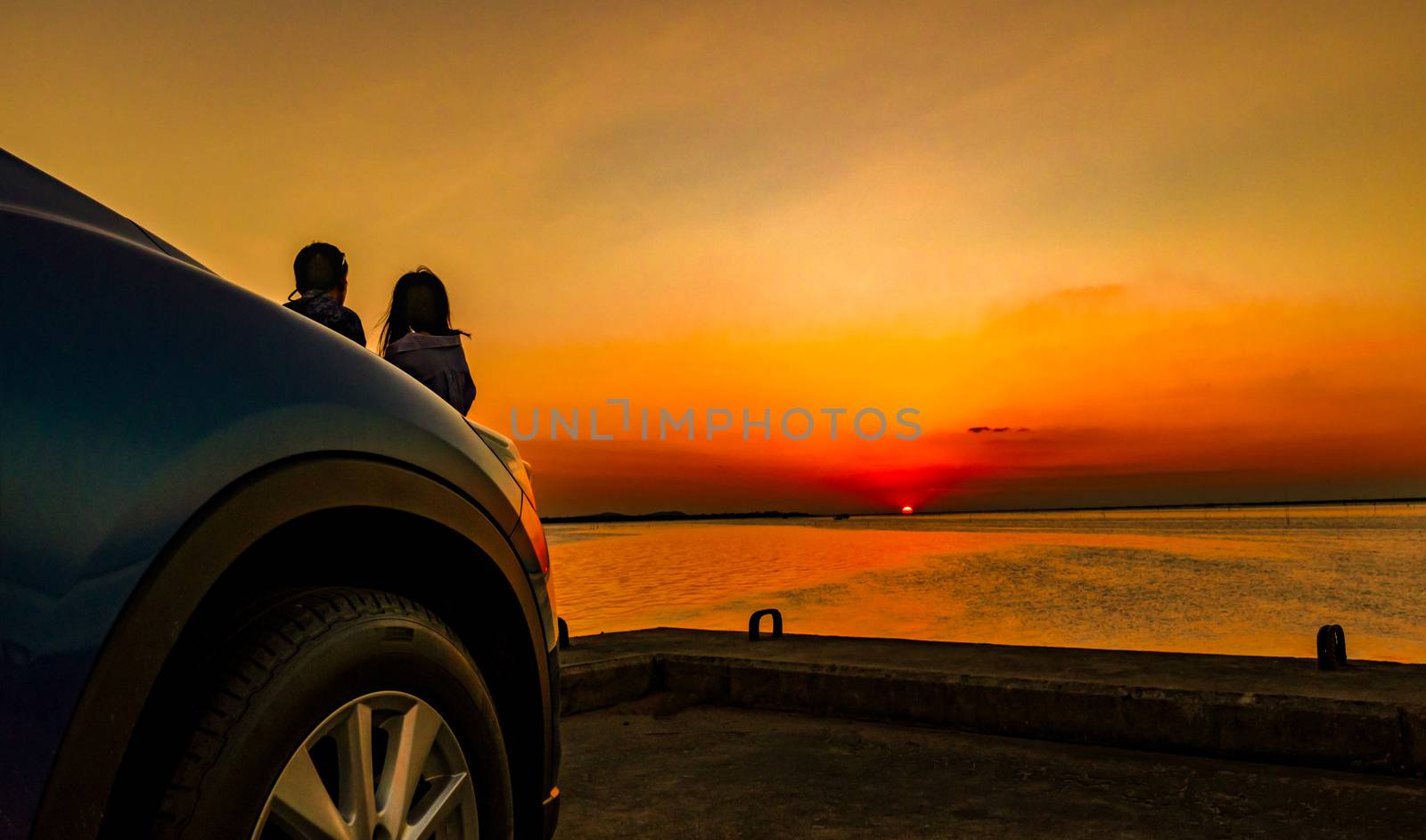 Silhouette of happiness couple standing and relaxing on the beach in front of the car with orange and blue sky at sunset. Summer vacation and travel concept. Romantic young couple dating at seaside. by Fahroni