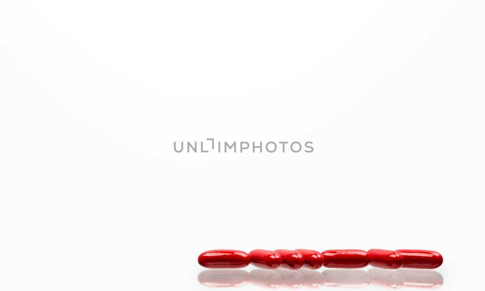 Red capsule pills isolated on white background with shadows and copy space for text. Vitamin and supplement for pregnancy and elderly people. Pharmaceutical industry. Pharmacy background. Global healthcare concept.