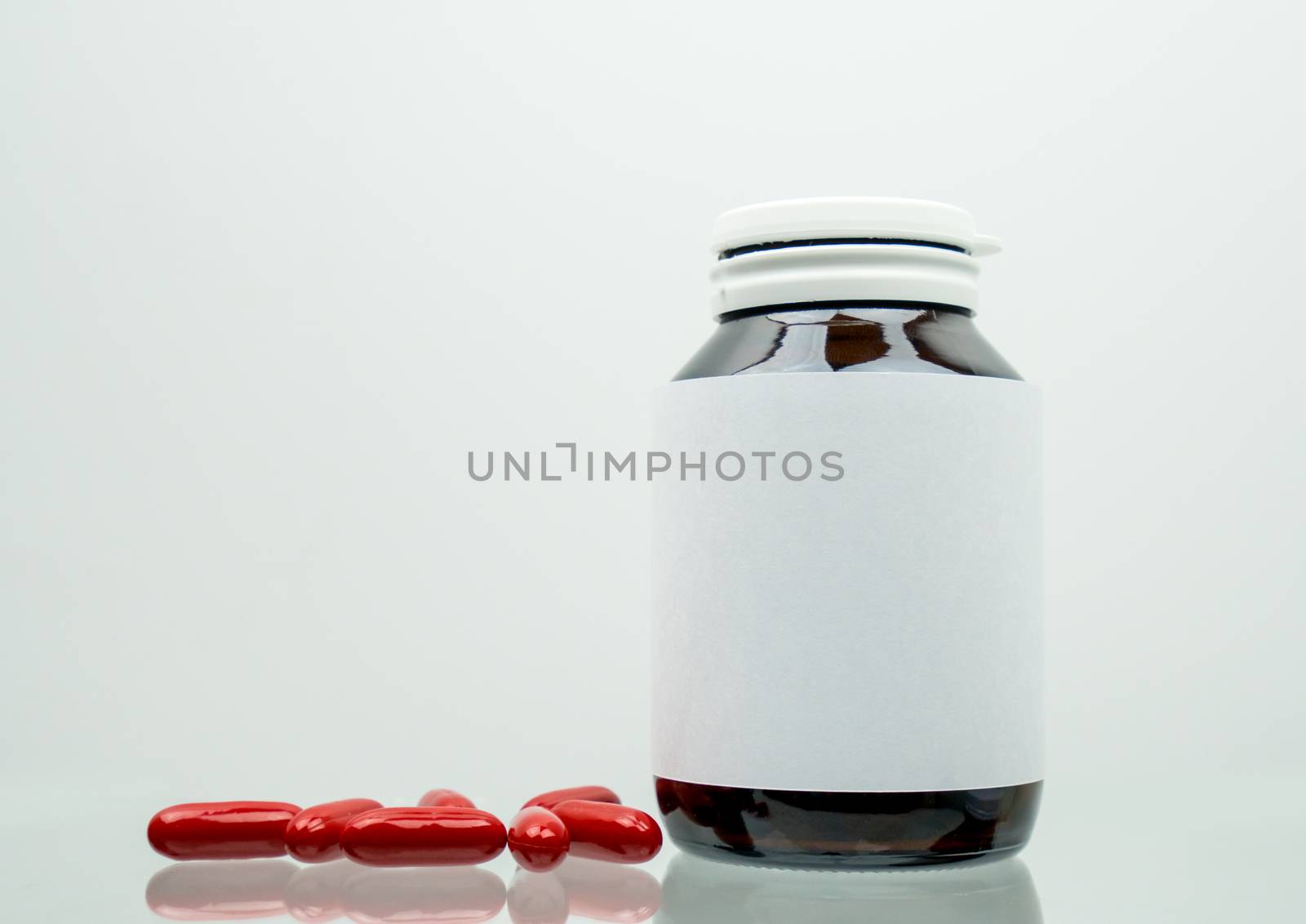 Red multivitamins capsule pills for pregnant woman with amber bottle and blank label and copy space isolated on white background. Vitamin and supplement for pregnancy and elderly people. Pharmaceutical industry. Pharmacy background.