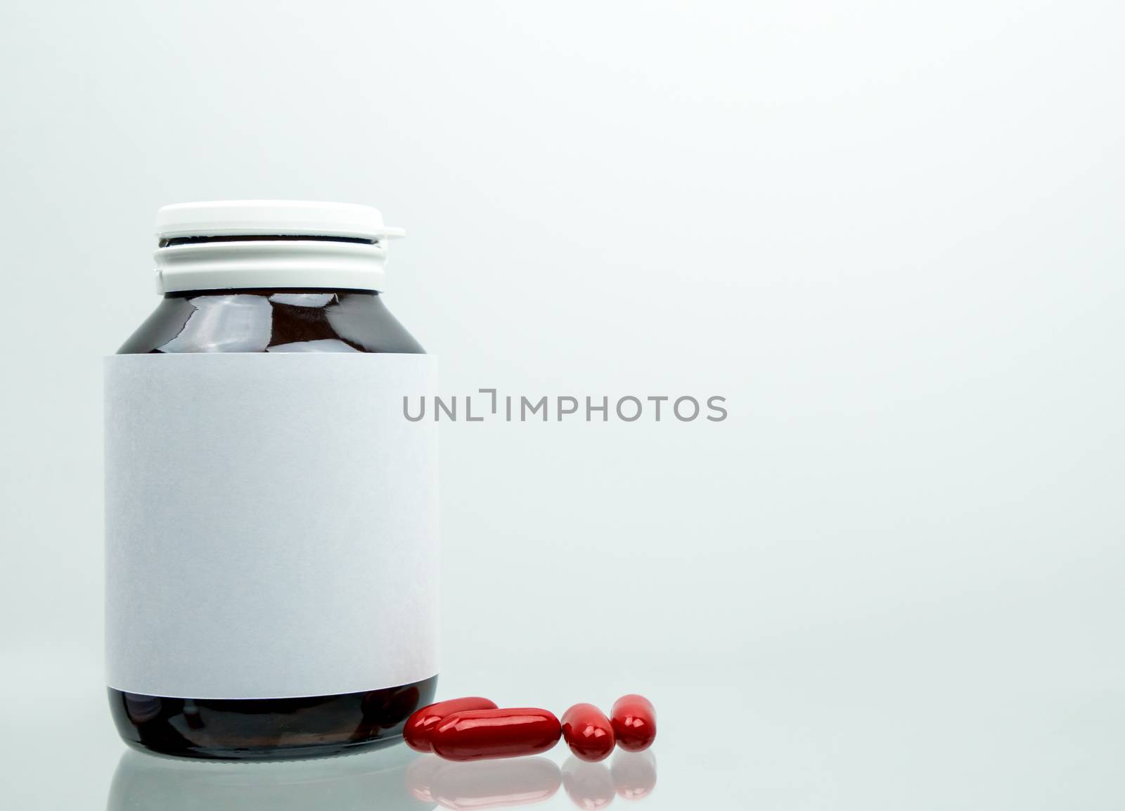 Macro shot of red multivitamins capsule pills for pregnant woman with amber bottle and blank label and copy space isolated on white background. Vitamin and supplement for pregnancy and elderly people. Pharmaceutical industry. Pharmacy background.