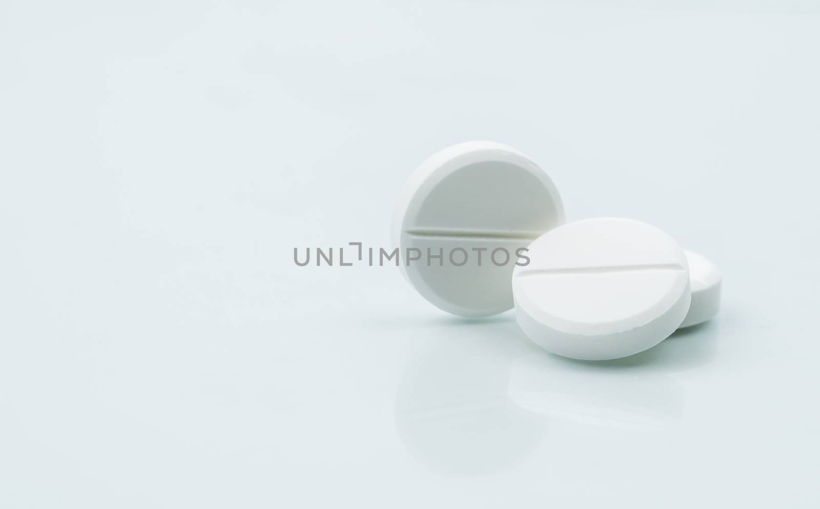 Macro shot of three white chewable tablets on white background with shadows. Antacids pills for relief stomachache from excess gastric acid in stomach. Stress induce gastric ulcer treatment concept. by Fahroni