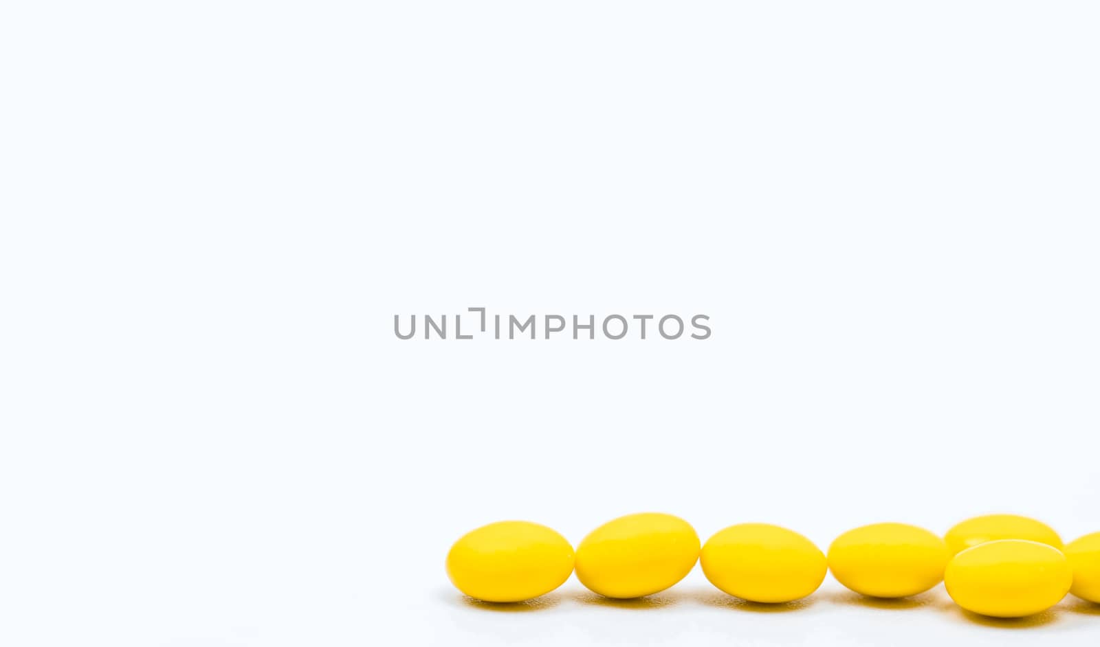 Yellow sugar coated tablets pills on white background with copy space. Medicine for treatment constipation. Pharmaceutical industry. Pharmacy background. Global healthcare concept. Health budgets and policy.