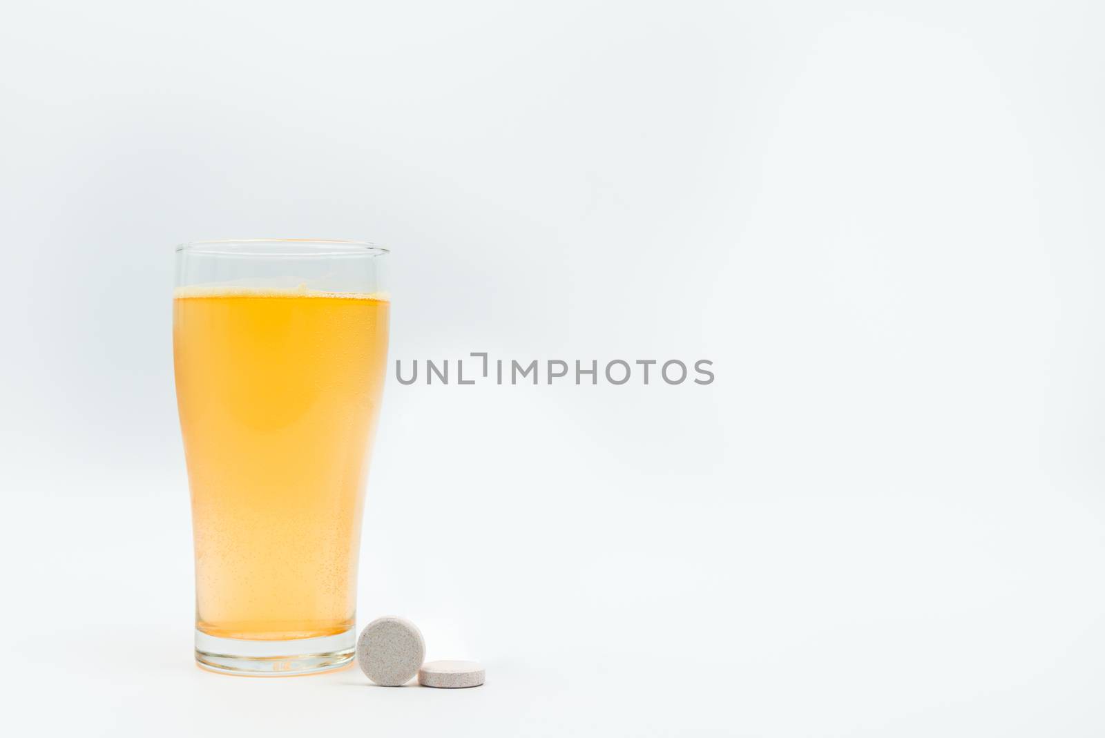 Two effervescent tables on white background and orange effervescent bubbles of calcium and vitamin C effervescent tablets in transparent glass. Vitamins, minerals and supplement concept.