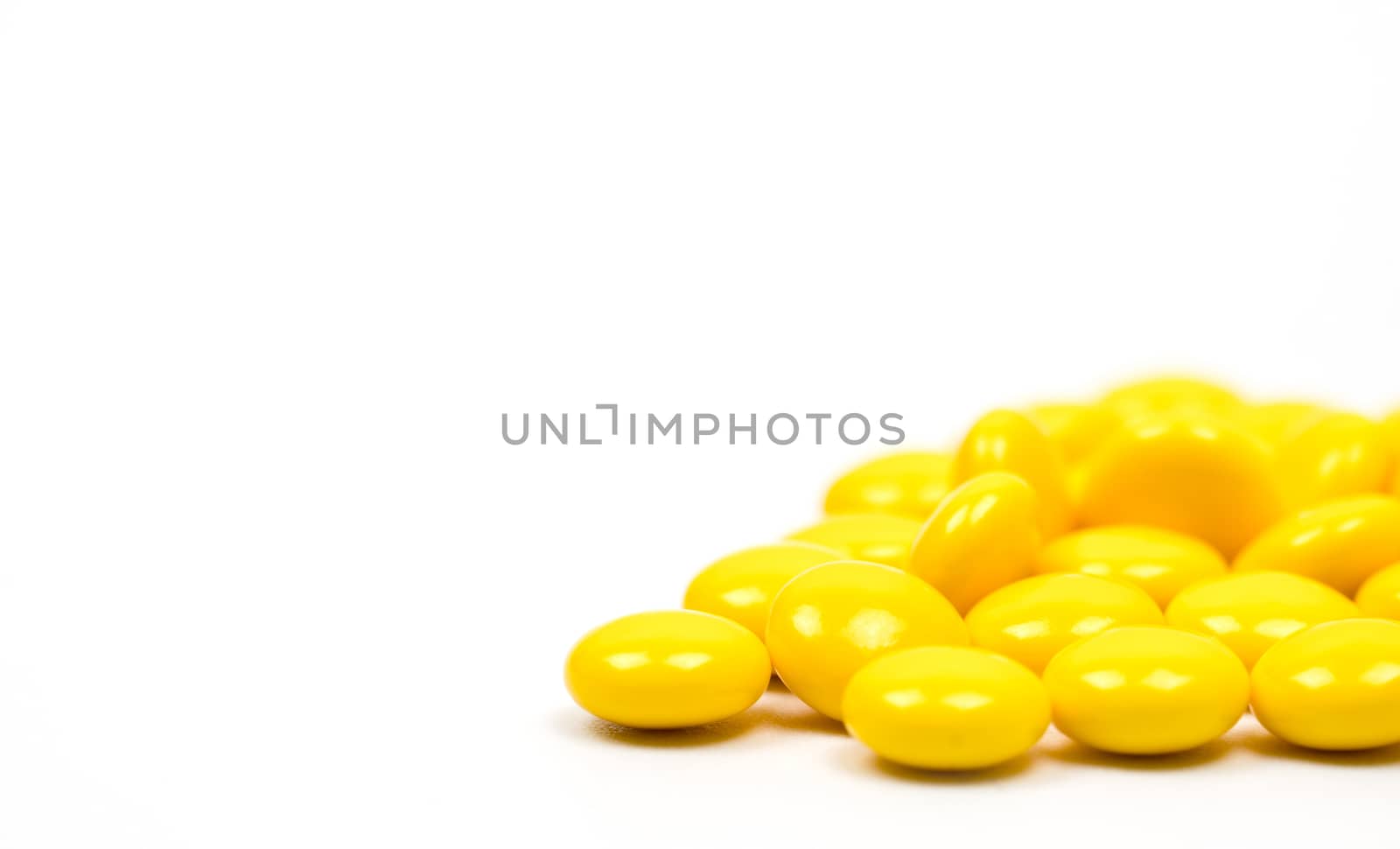Yellow sugar coated tablets pills on white background with copy space. Medicine for treatment constipation. Pharmaceutical industry. Pharmacy background. Global healthcare concept. Health budgets and policy.
