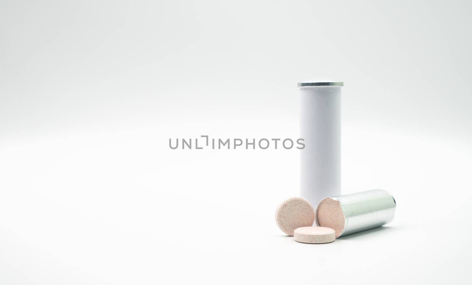 Effervescent tables tube with blank label and copy space on white background. Calcium and vitamin C effervescent tablets are removed from the foil packaging. Vitamins, minerals and supplement concept. by Fahroni