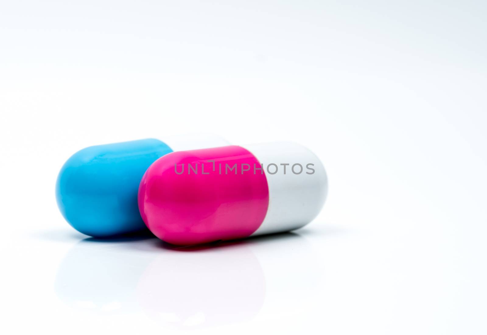 Two capsule pills isolated on white background. Global healthcare concept. Pharmacy sign and symbol. Pharmaceutical industry. Pharmacy background. Global healthcare concept. Antibiotic or antimicrobial drug resistance. Health budgets and policy. Blue-white and pink-white antibiotic capsule.