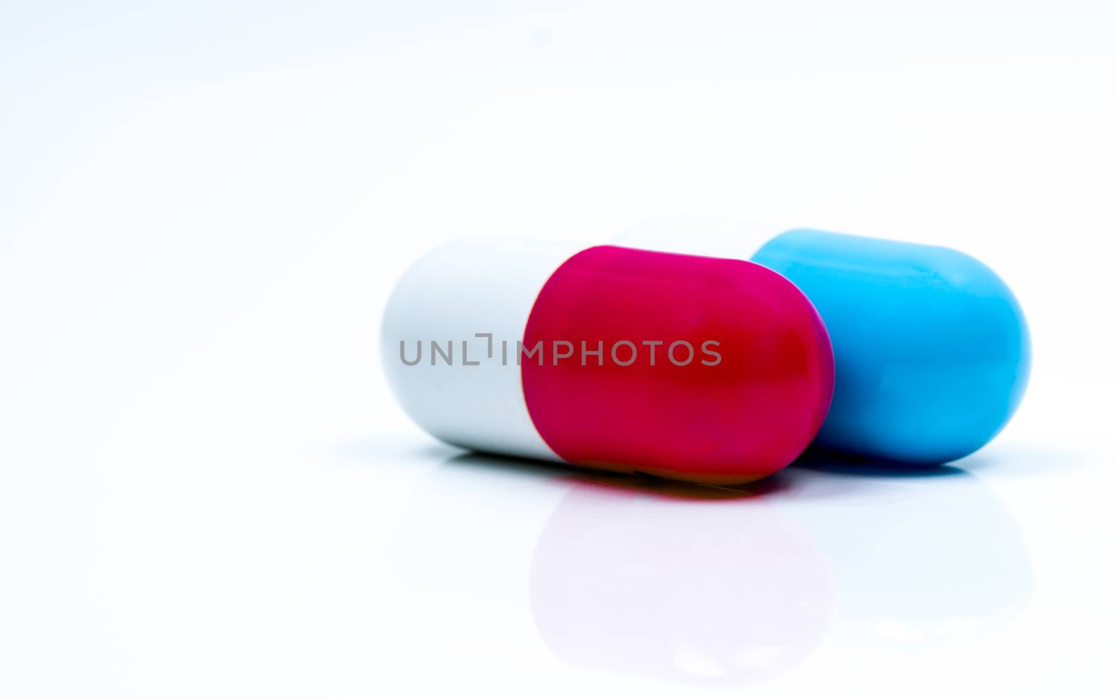 Two capsule pills isolated on white background. Global healthcare concept. Pharmacy sign and symbol. Pharmaceutical industry. Pharmacy background. Global healthcare concept. Antibiotic or antimicrobial drug resistance. Health budgets and policy. Blue-white and red-white antibiotic capsule. by Fahroni
