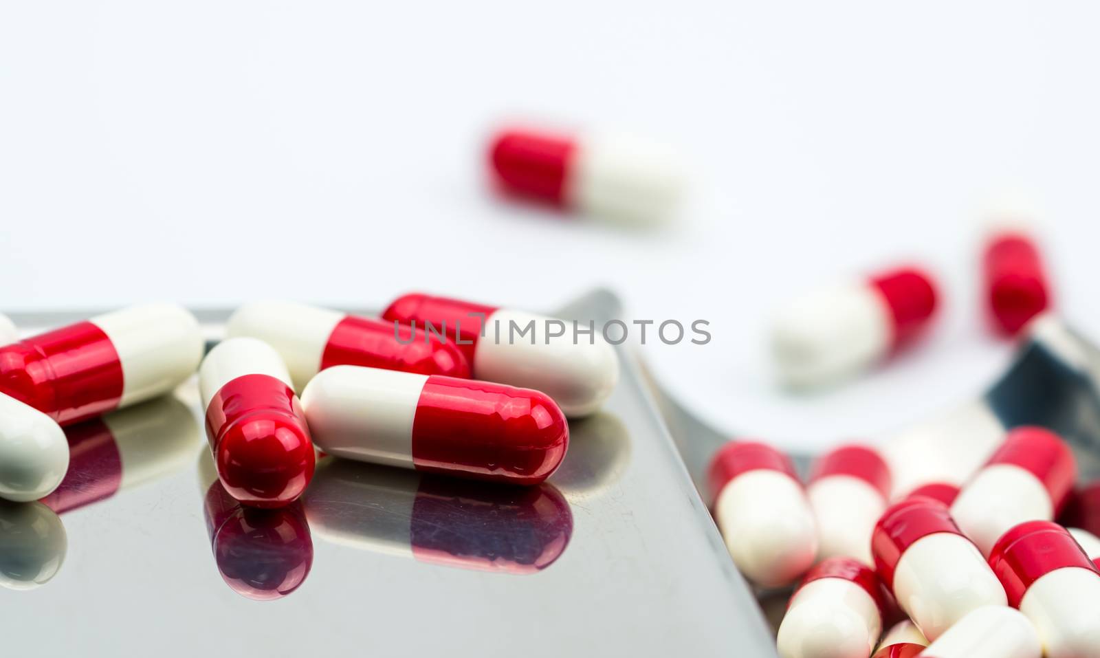 Red, white antibiotic capsules pills on stainless steel drug tray. Drug resistance, antibiotic drug use with reasonable, health policy and health insurance concept. Pharmaceutical industry. Pharmacy background.