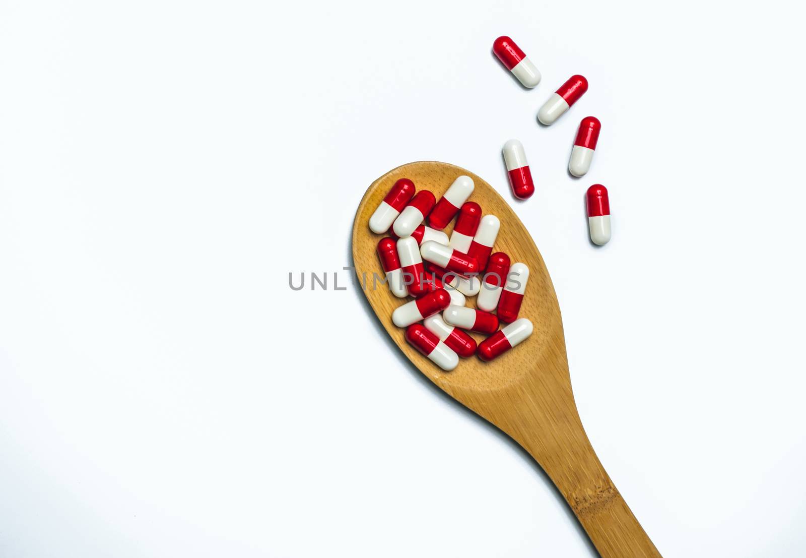 Colorful of antibiotics capsule pills in wooden spoon are spilling on white background with copy space. Antibiotic drug use with reasonable and health insurance concept. Pharmaceutical industry. Pharmacy background. Antimicrobial overuse. Health budgets and policy.