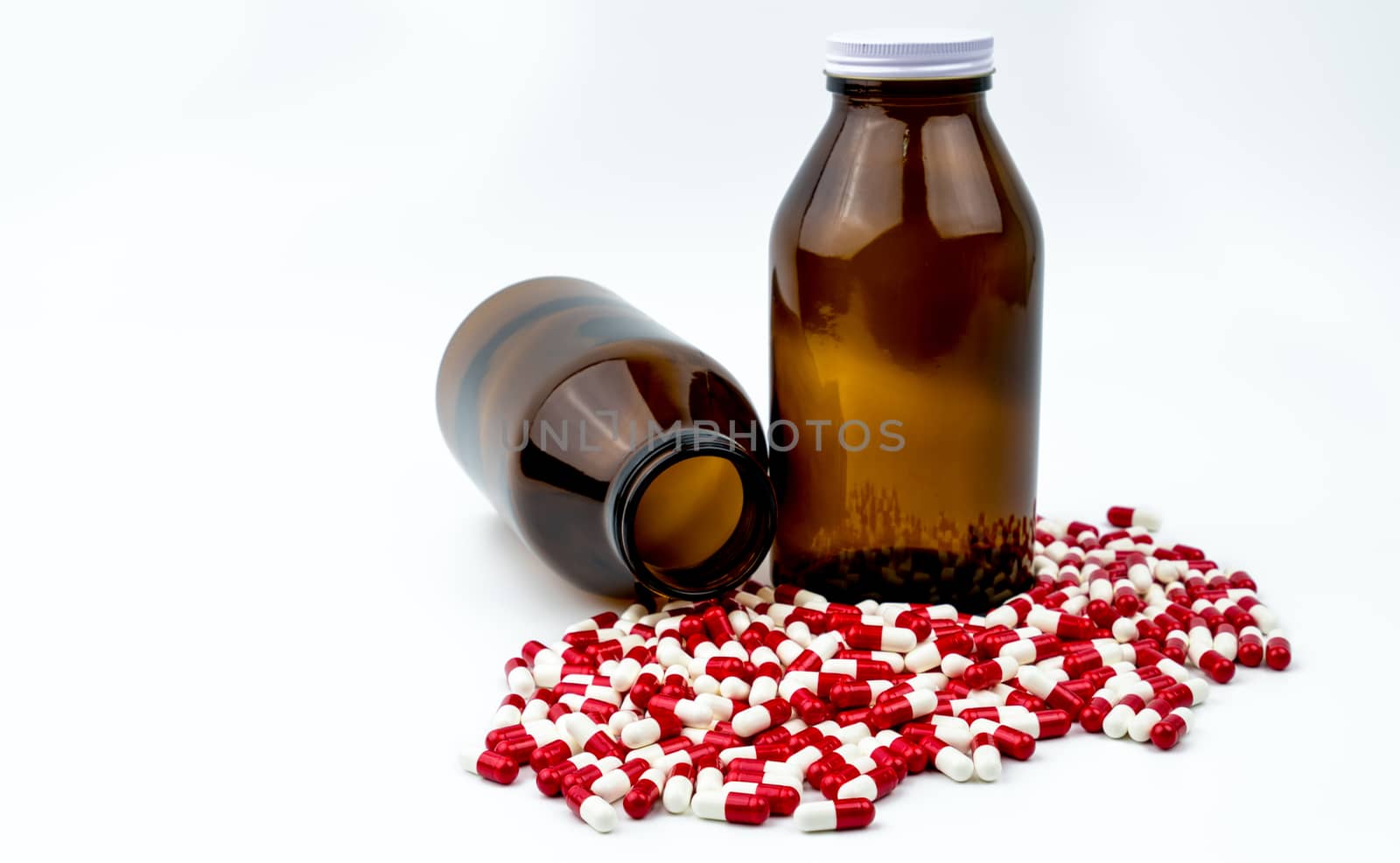 Colorful of antibiotic capsules pills with two amber glass bottles isolated on white background. Drug resistance, antibiotic drug use with reasonable. Pharmaceutical industry. Pharmacy background. Antibiotics drug overuse. Health budgets and policy.