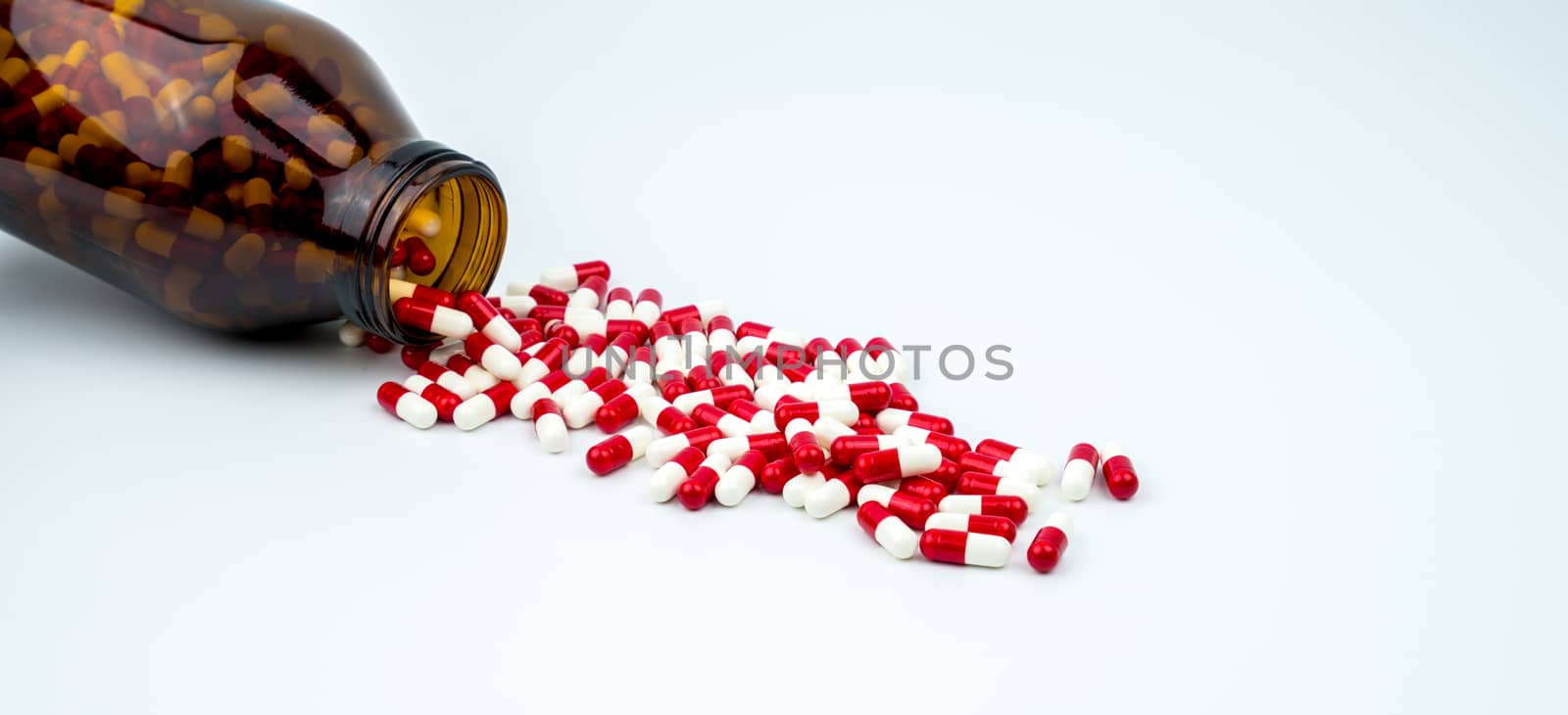 Colorful of antibiotic capsules pills with two amber glass bottles isolated on white background. Drug resistance, antibiotic drug use with reasonable. Pharmaceutical industry. Pharmacy background. Antibiotics drug overuse. Health budgets and policy. by Fahroni