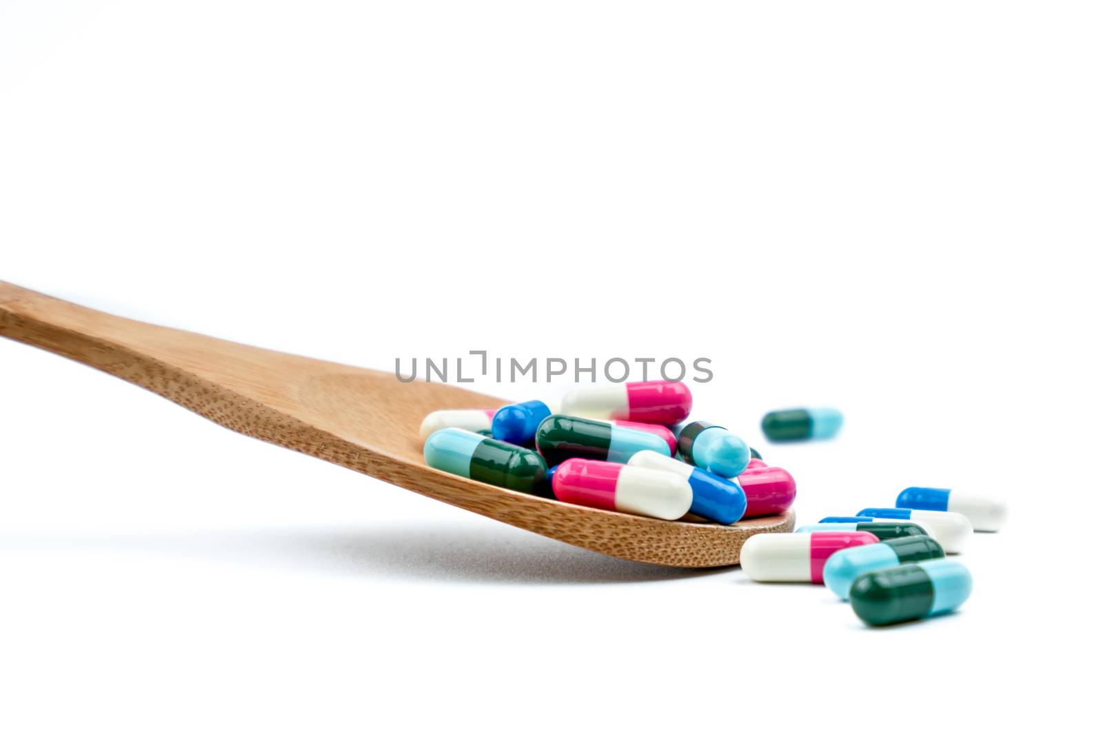 Colorful of antibiotics capsule pills in wooden spoon are spilling on white background with copy space. Antibiotic drug use with reasonable. Pharmaceutical industry. Pharmacy background. Health budgets and policy. Antimicrobial drug overuse. by Fahroni