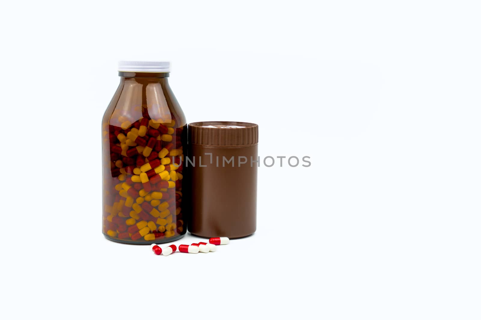Red, white antibiotic capsules pills and two amber bottles isolated on white background with copy space and blank label. Drug resistance, antibiotic drug use with reasonable. Pharmaceutical industry. Pharmacy background. Health budgets and policy.