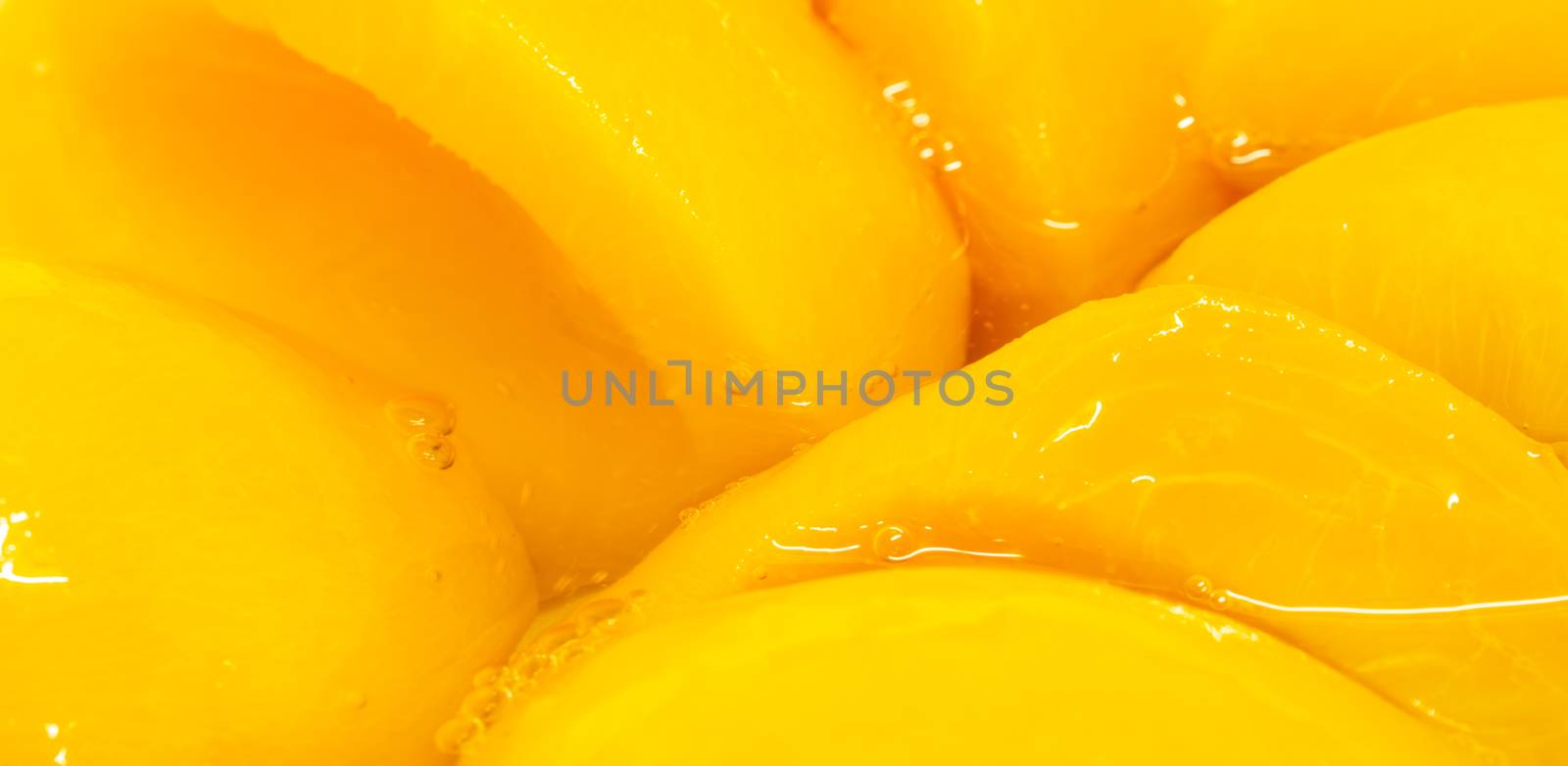 Closeup canned peach halves in syrup. Yellow fruit.