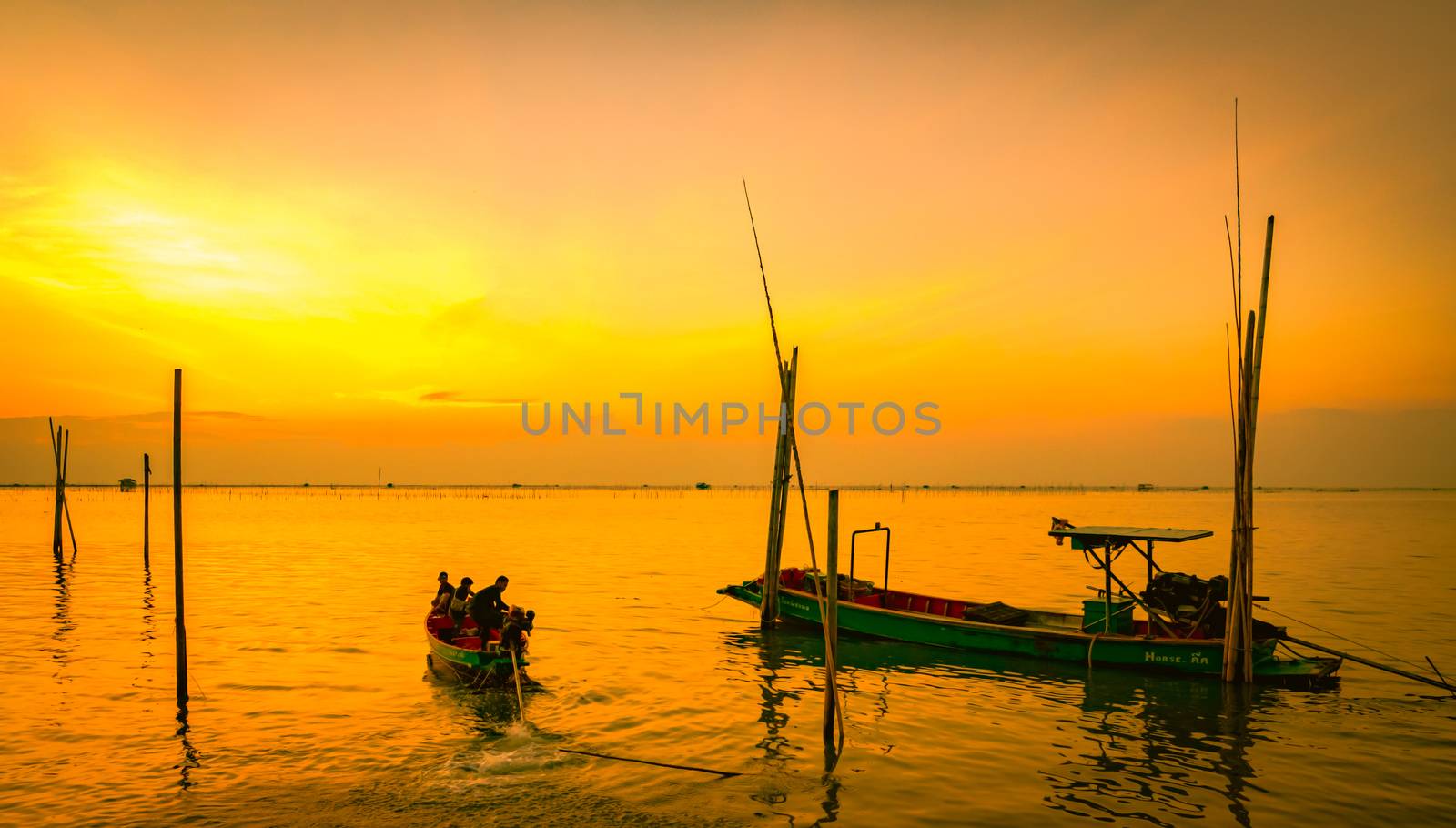 Fisherman's boat floating in the sea near bamboo pole at sunset in Thailand.