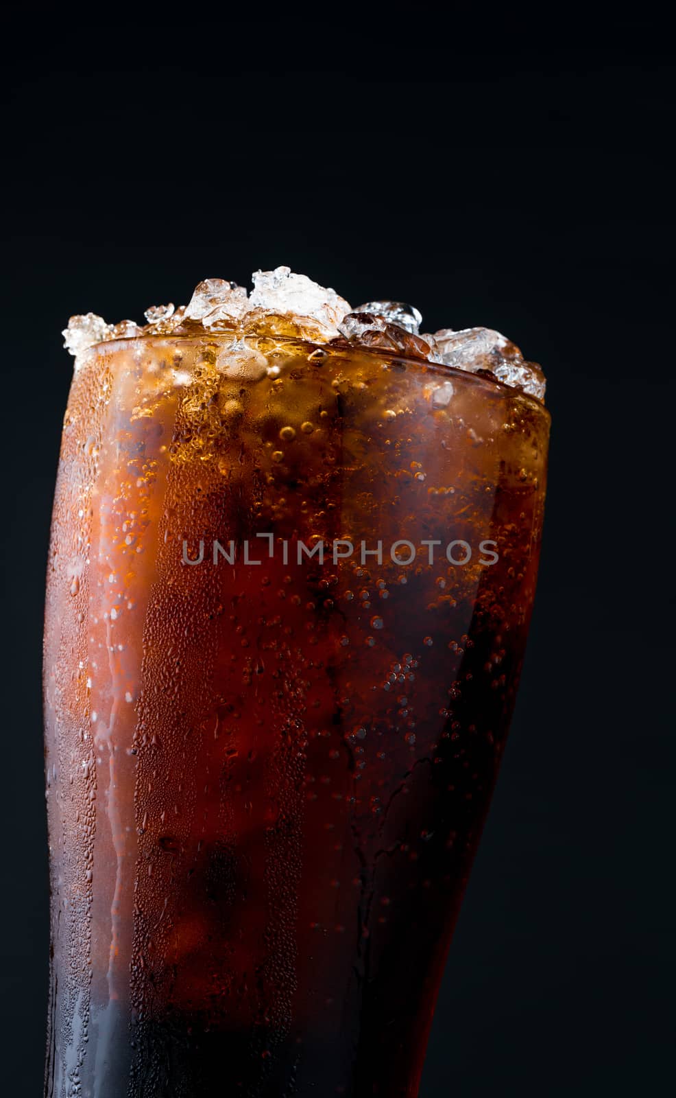 Soft drink with ice in glass isolated on dark background with copy space. There is a drop of water on the transparent glass surface.