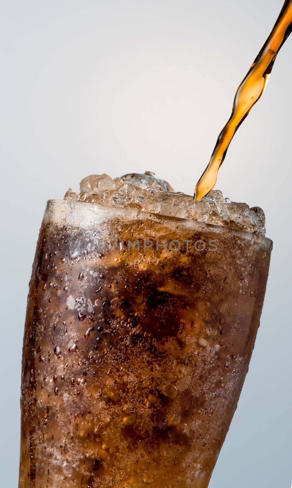 Closeup of soft drink pouring to glass with crushed ice cubes isolated on white background with copy space. There is a drop of water on the transparent glass surface. by Fahroni