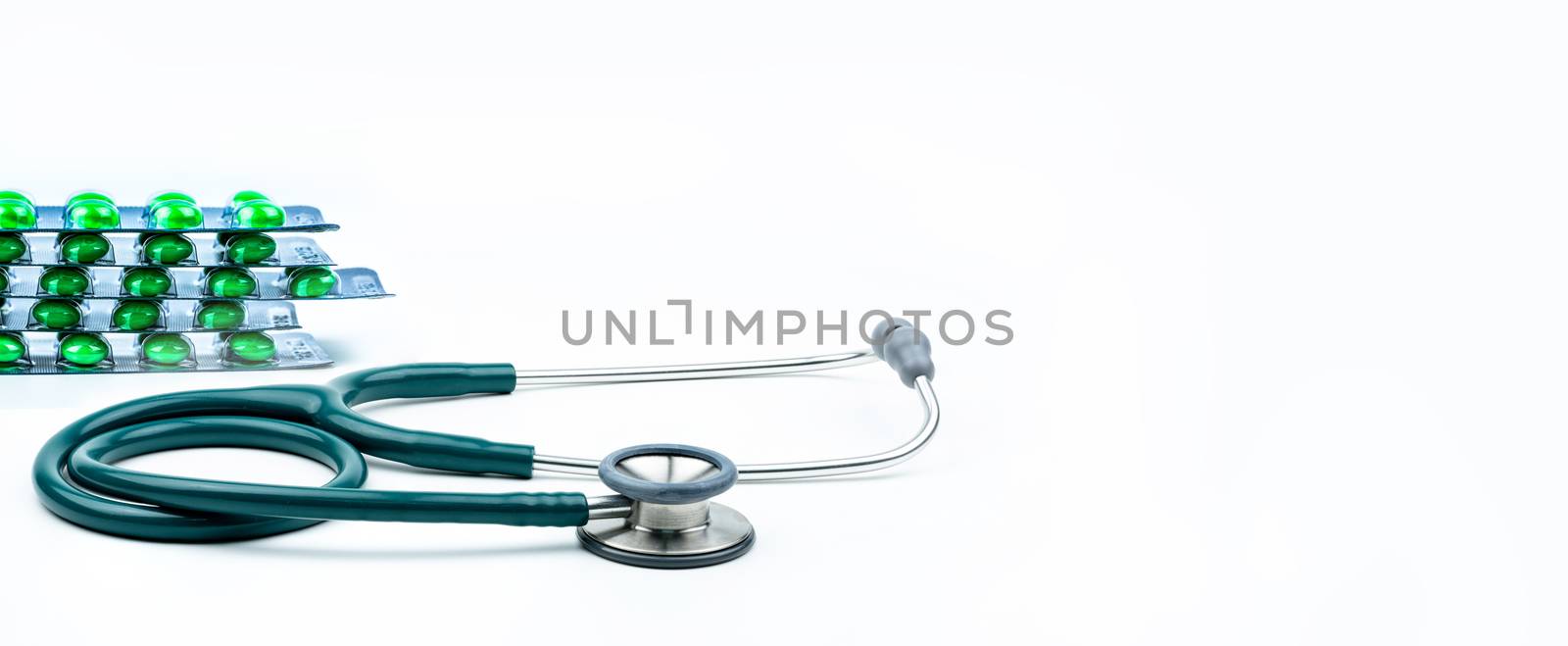 Stethoscope and green pills in blister pack isolated on white background with copy space. Medical tool for doctor. Health check up concept. Medical research background. Clinical Cardiology concept