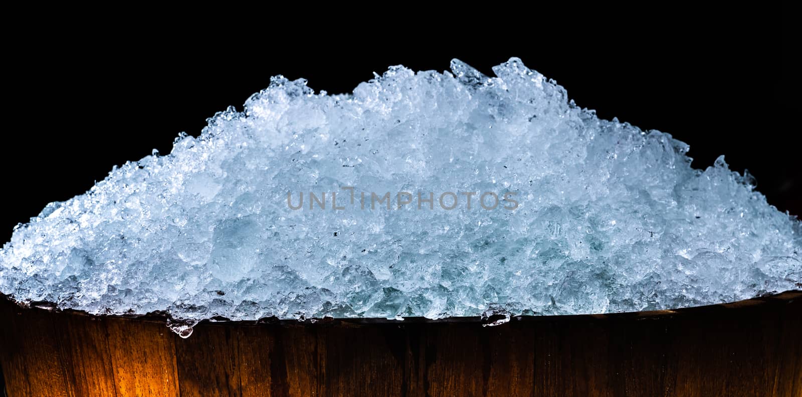 Pile of crushed ice cubes in wood bucket on dark background with copy space. Crushed ice cubes foreground for beverages, beer, whisky, fruit juice, milk, fresh food or fresh vegetables.