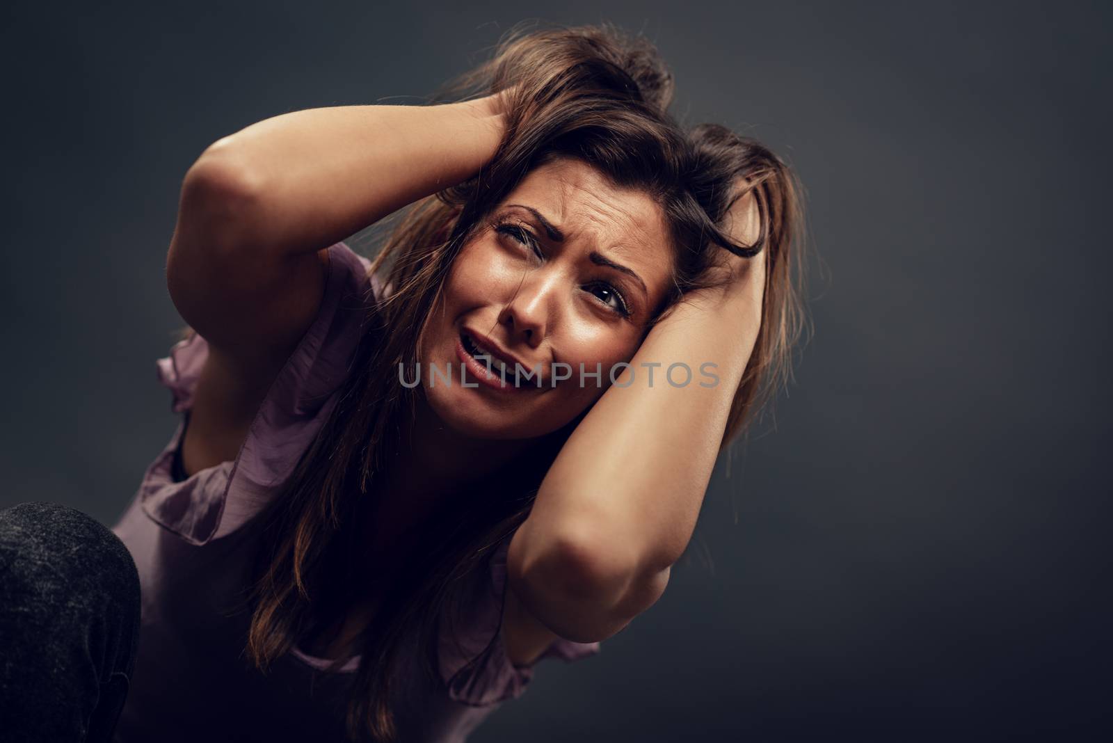 Young abused woman terrified looking with arms in her hair seeking safety.