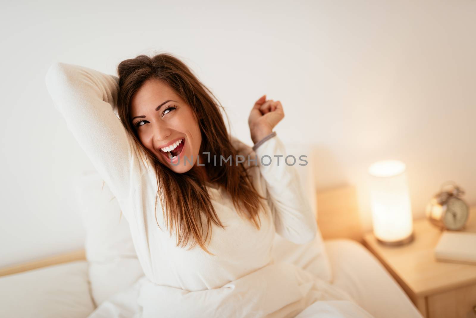 Young beautiful woman sitting in the bed in morning and stretching.