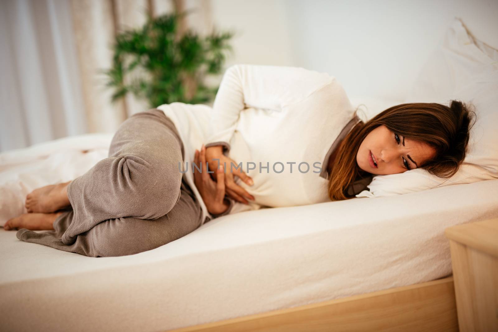 Beautiful young woman lying on bed and holding hands on her stomach.