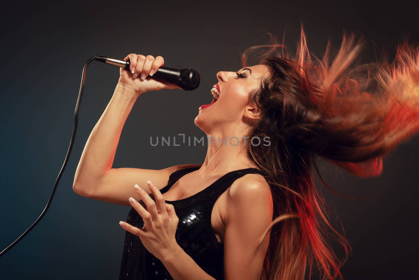 A young woman singer with tousled long hair holding a microphone and sing with a wide open mouth.