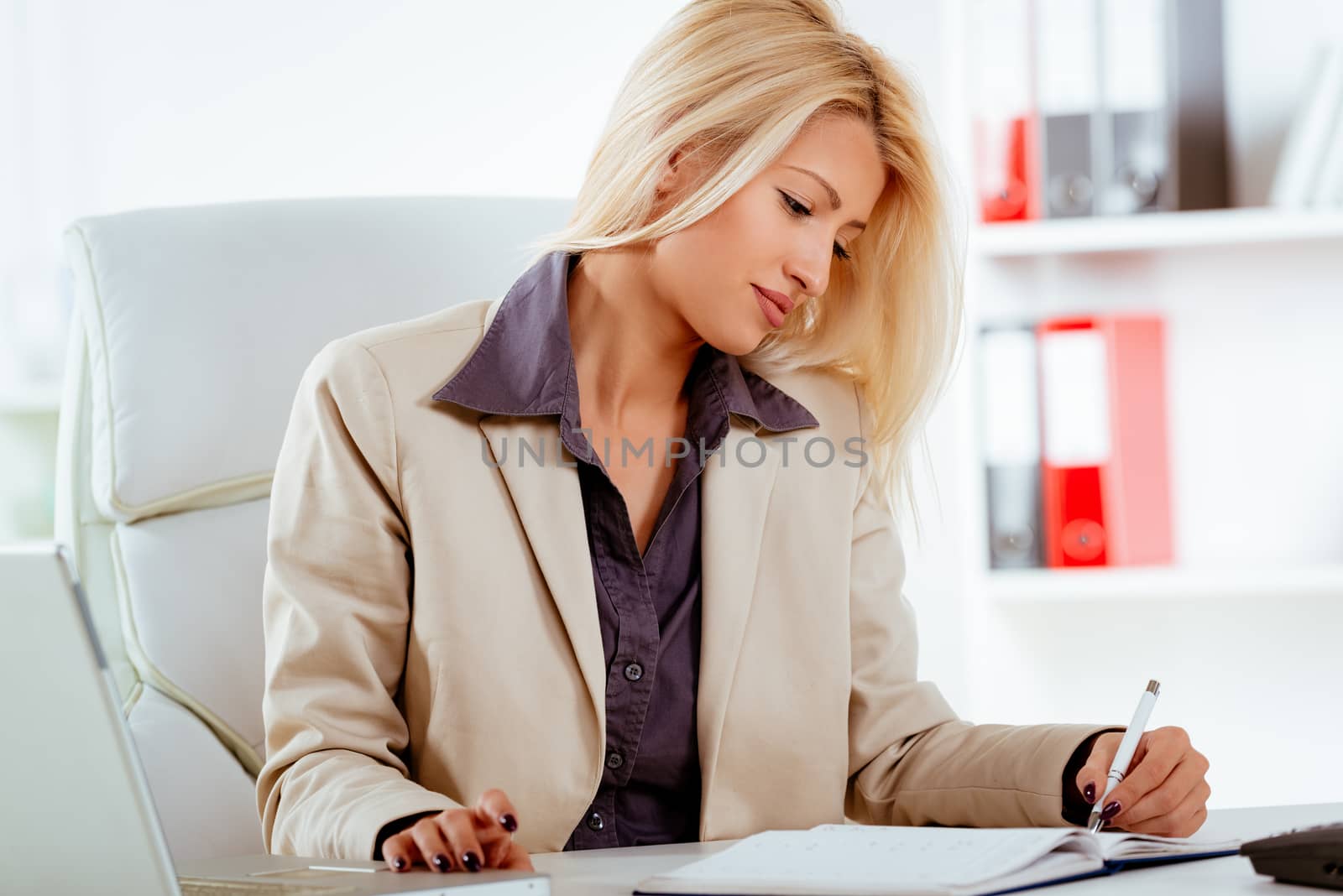 A young businesswoman sitting at the office and writing in planner with the left hand.