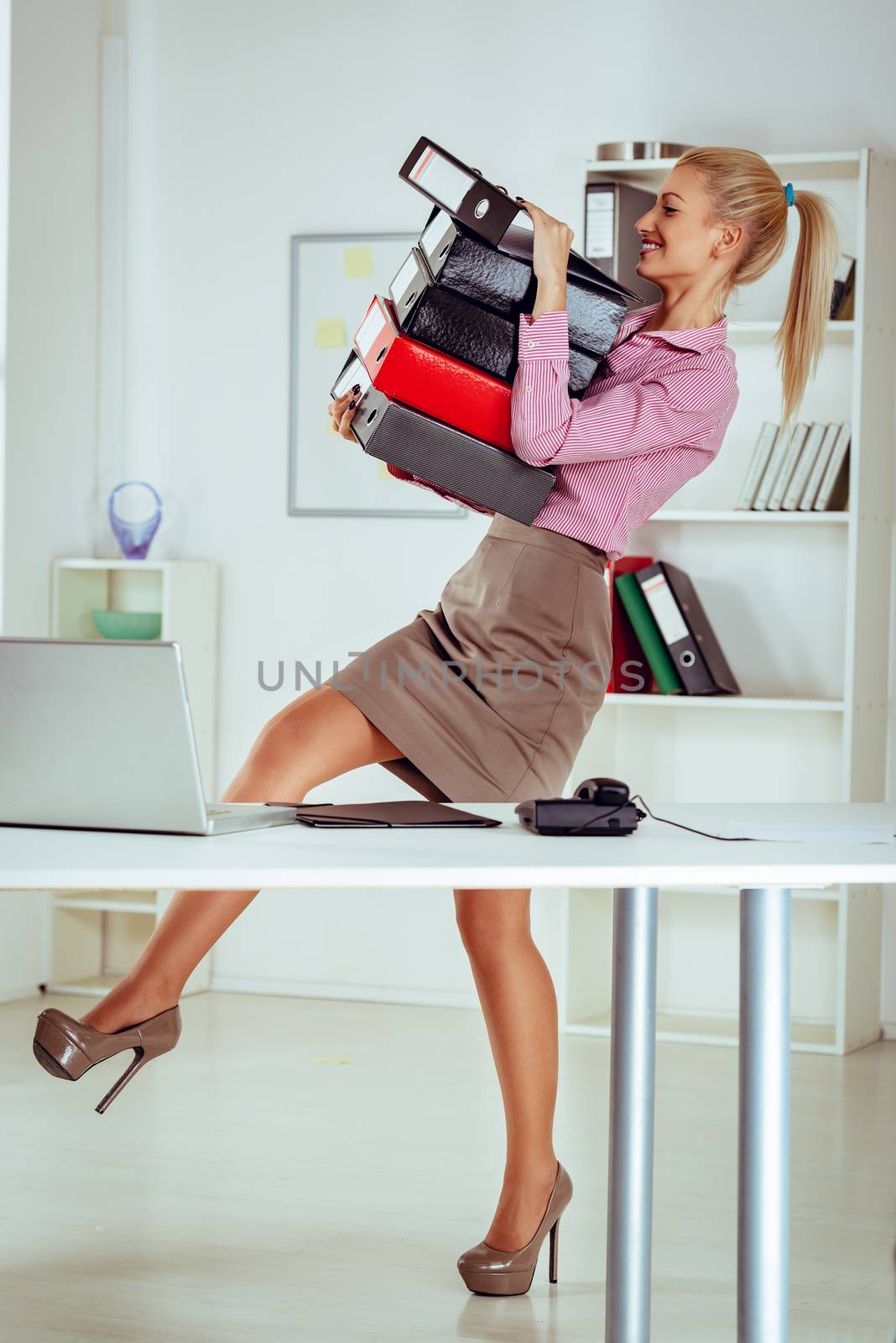 Young smiling business woman wearing a stack of binders in the hands and keep them not to fall.