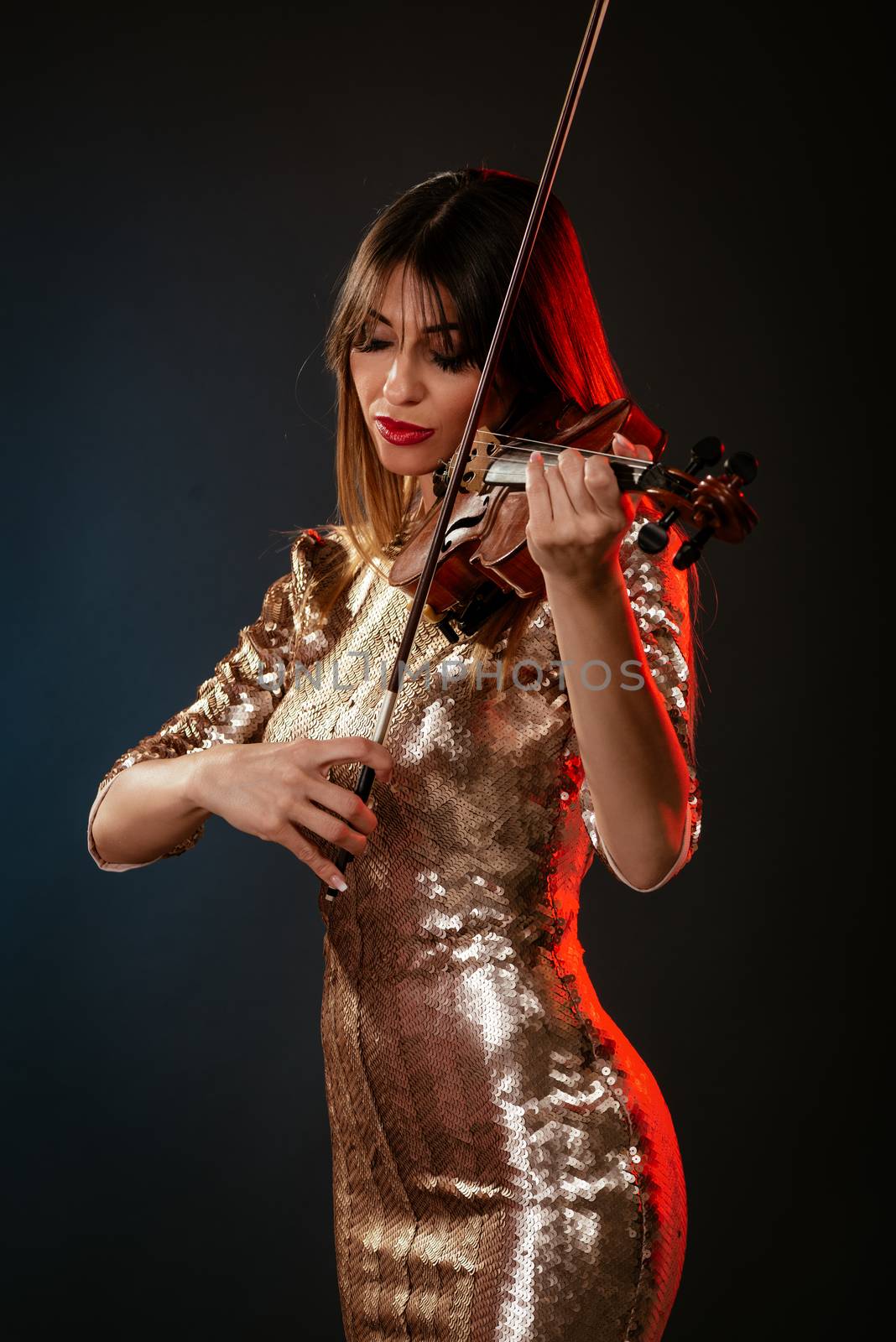 Beautiful young smiling woman in sequin dress playing the violin.
