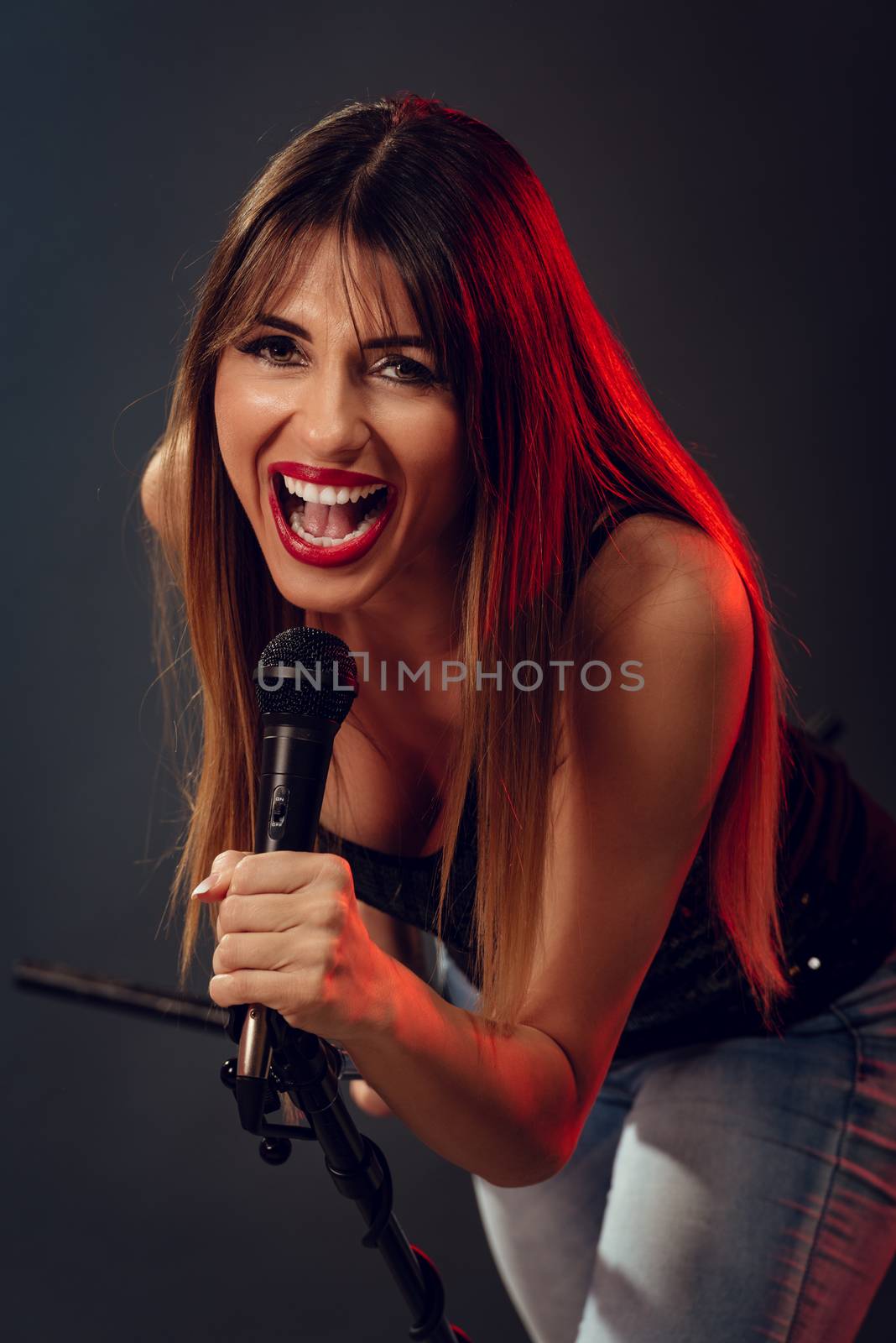 A young woman rock singer holding a microphone with stand and sing with a wide open mouth. Looking at camera.