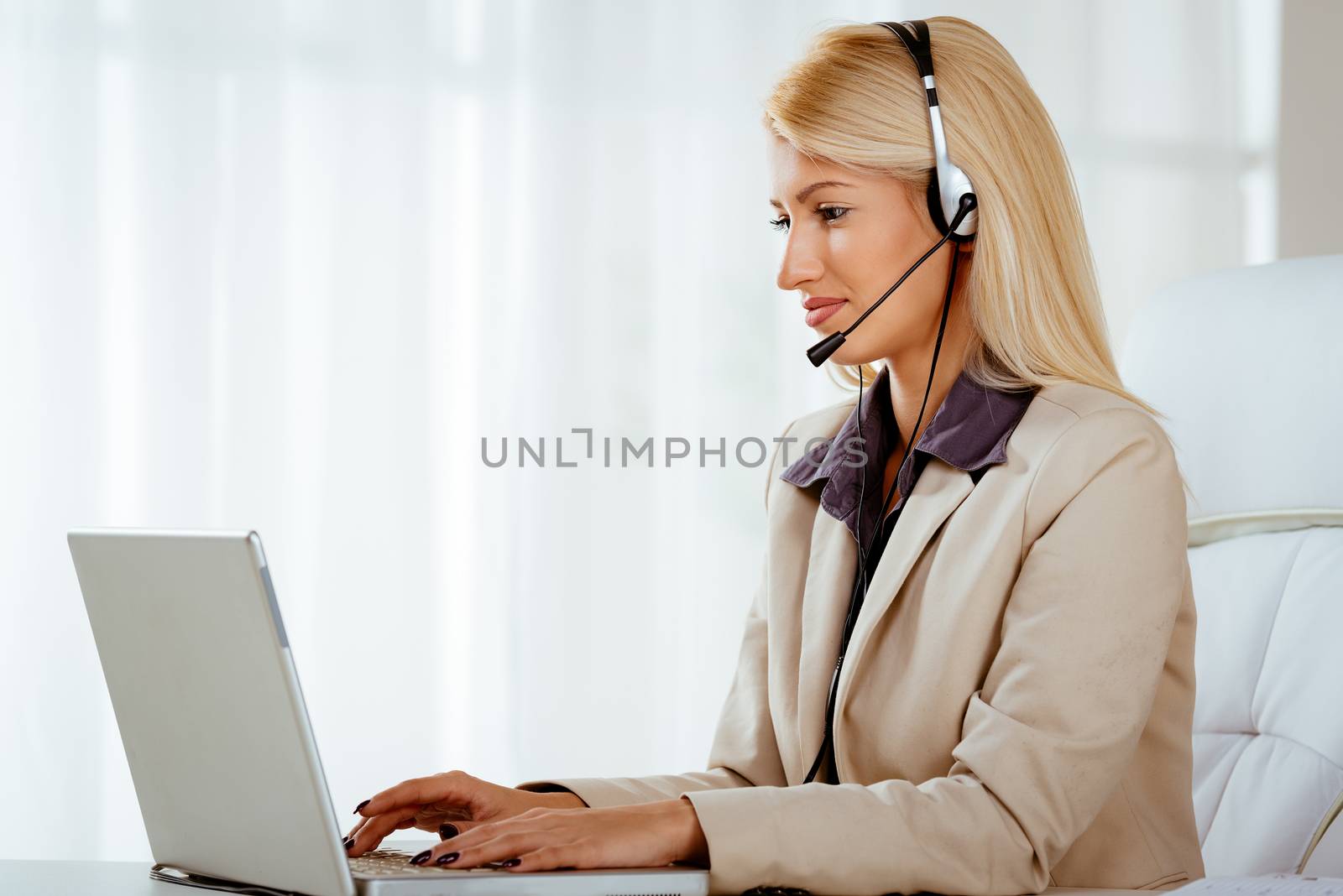 Beautiful smiling woman with a headset on her head using laptop at the office.